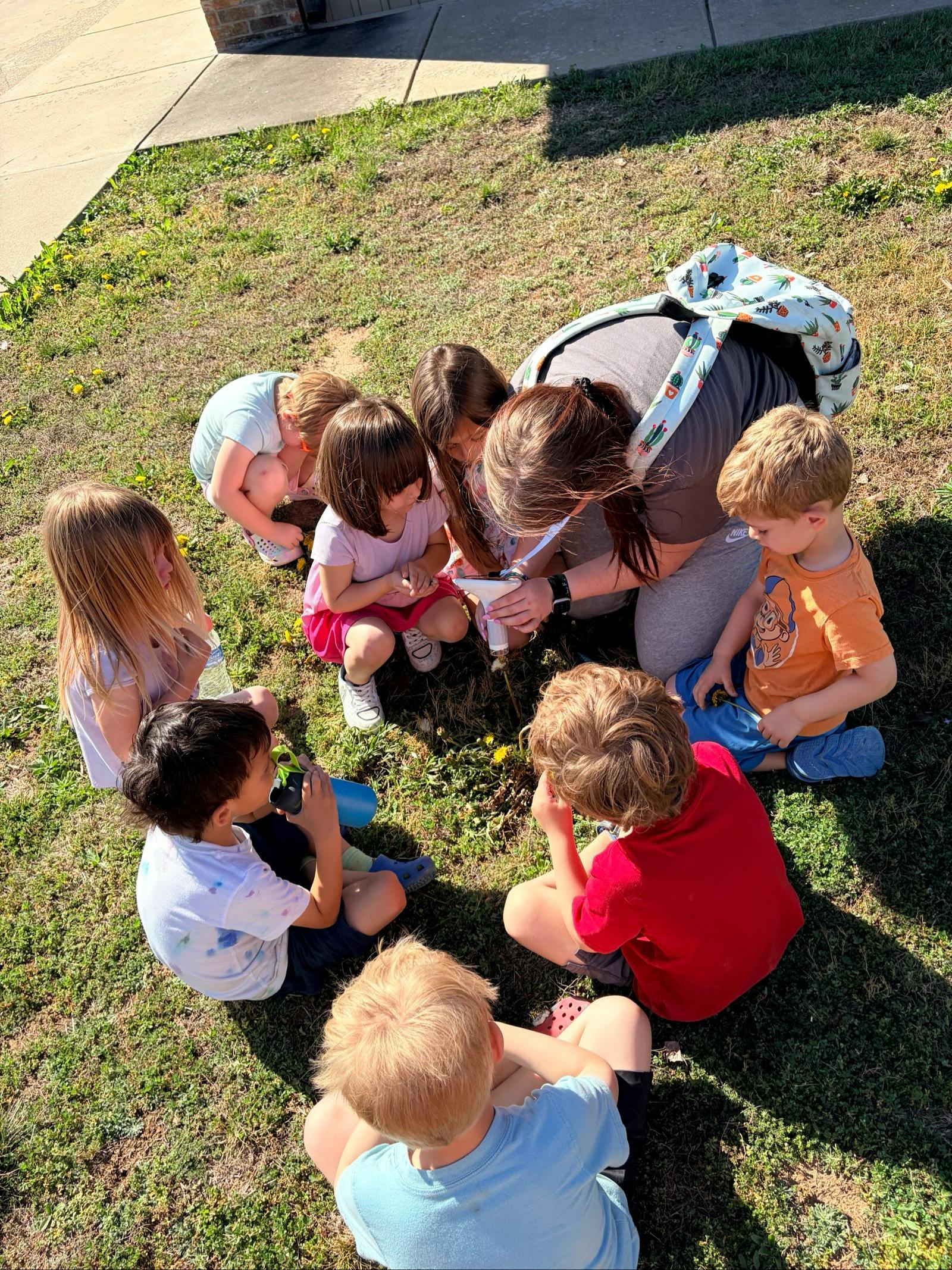 A person showing a group of children something on the ground through a viewer