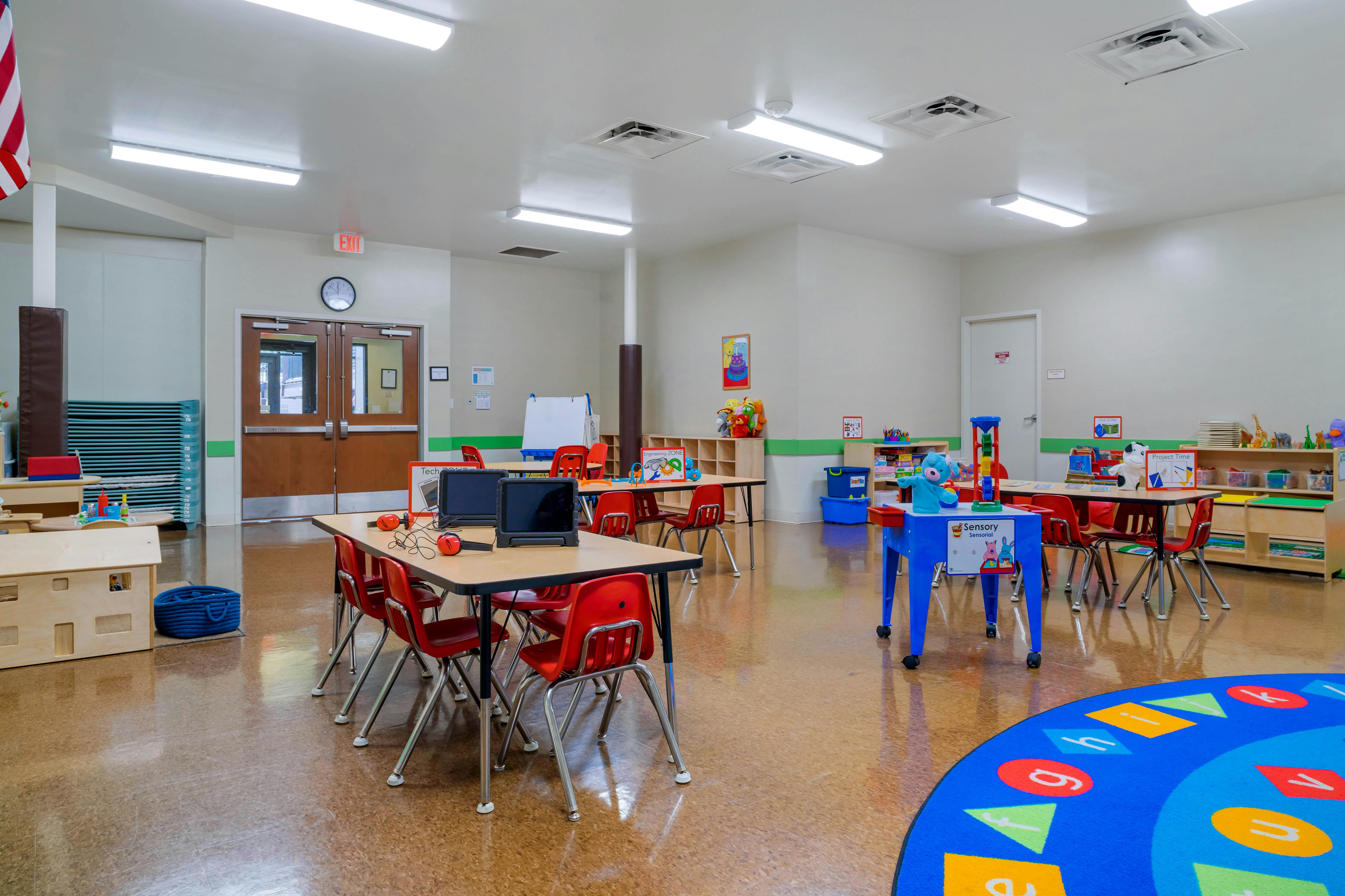Classroom with small tables, red chairs, and learning materials
