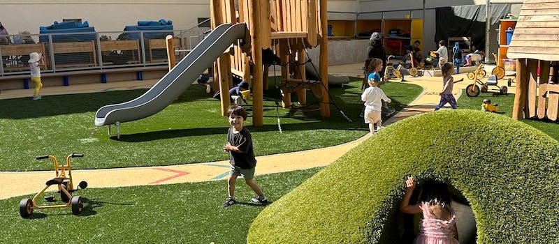 Children playing on a playground with a slide and grassy mounds