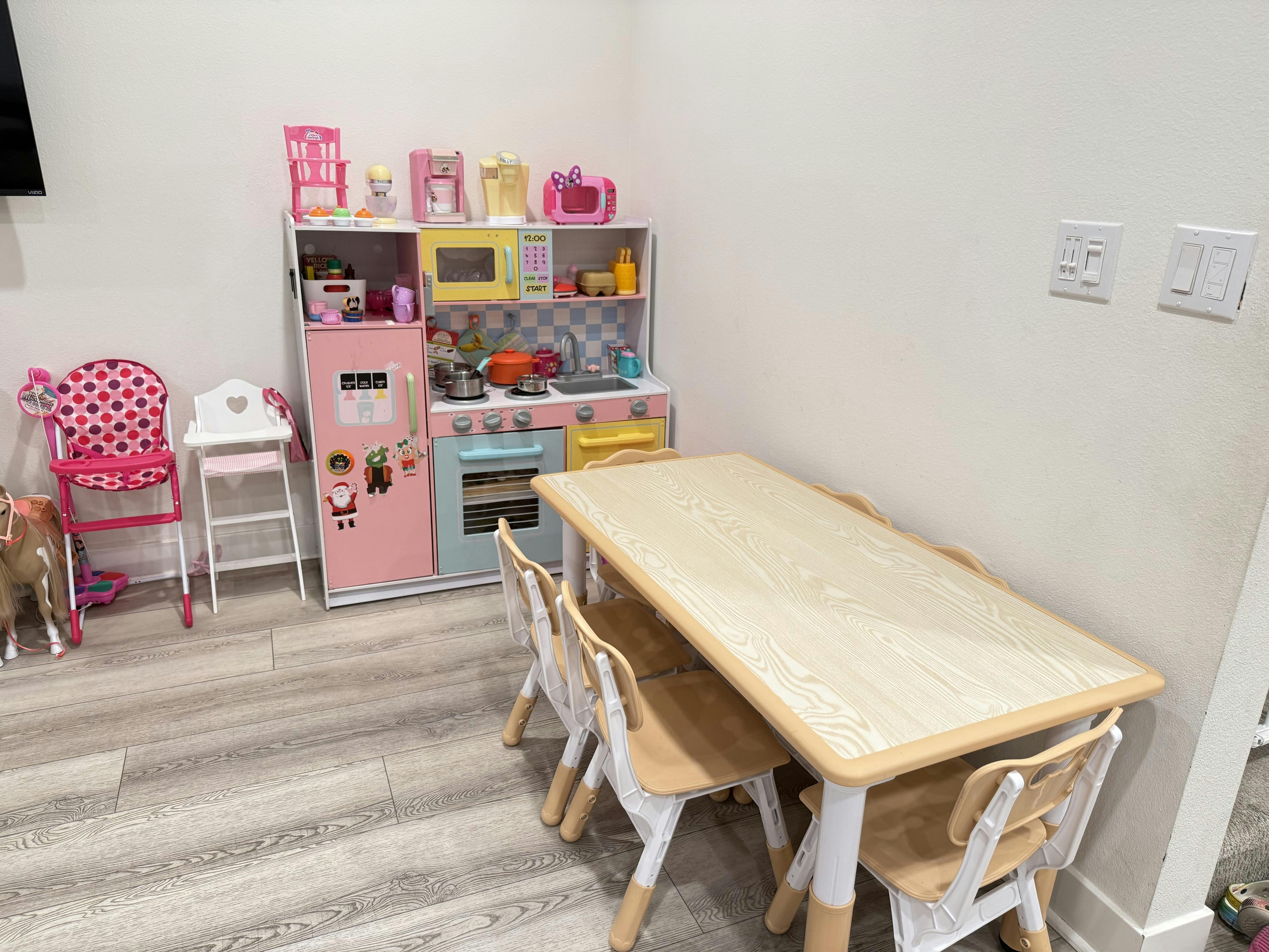 Child-sized table and chairs next to a pink toy kitchen set