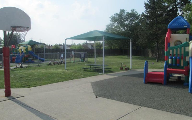 Playground area with swings, slide, and picnic tables under a shade canopy