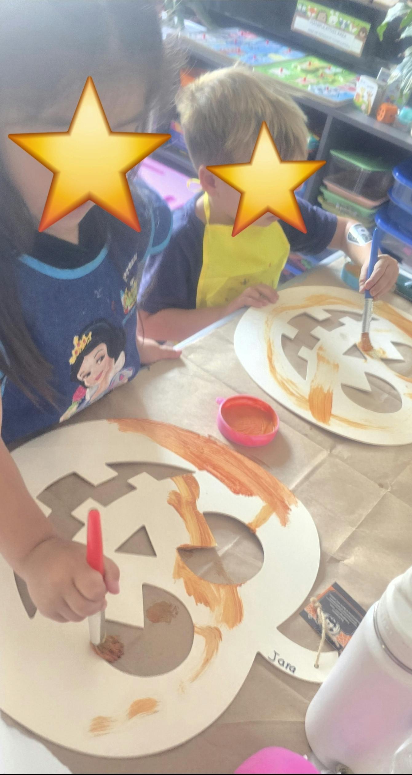 Two children painting pumpkin cutouts