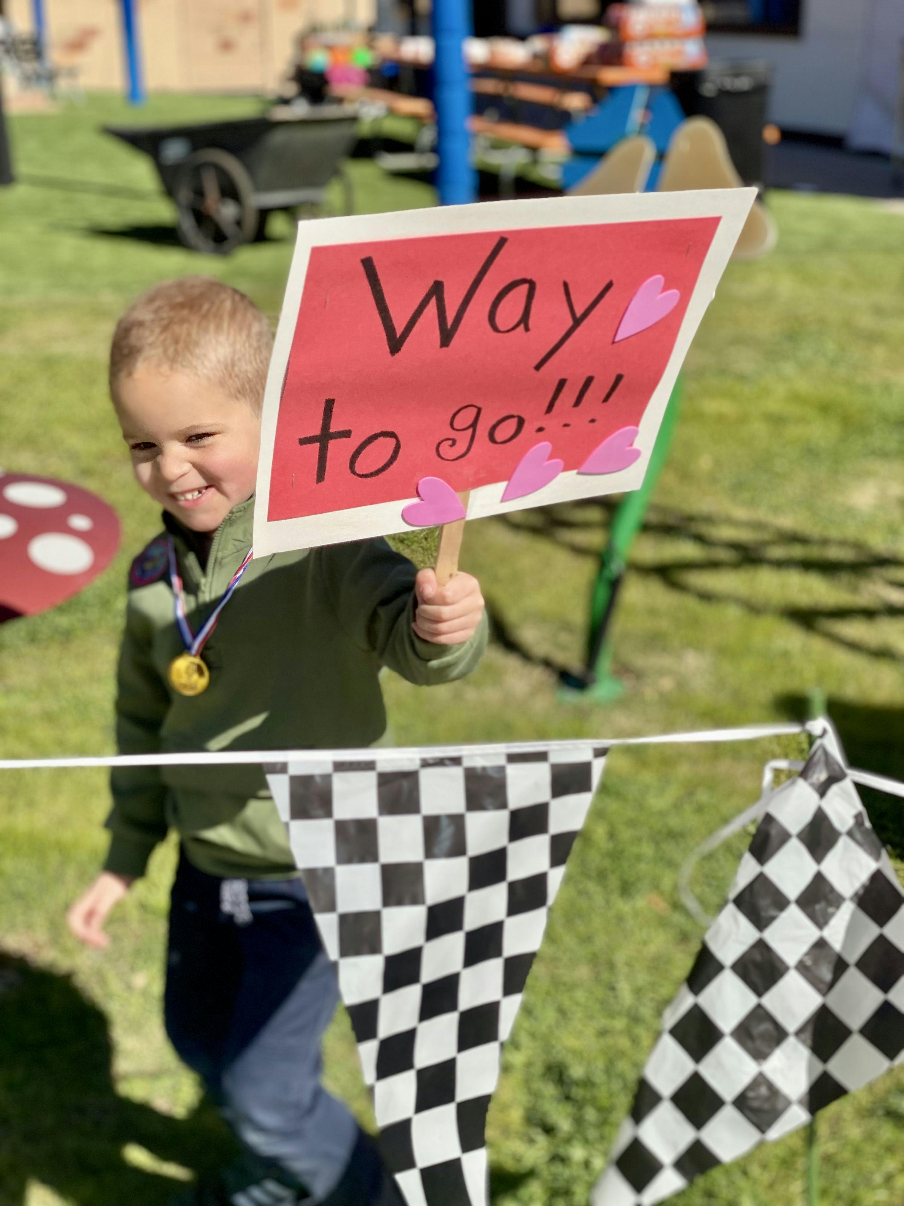 Child holding a sign that says "Way to go!!!" with a medal around their neck