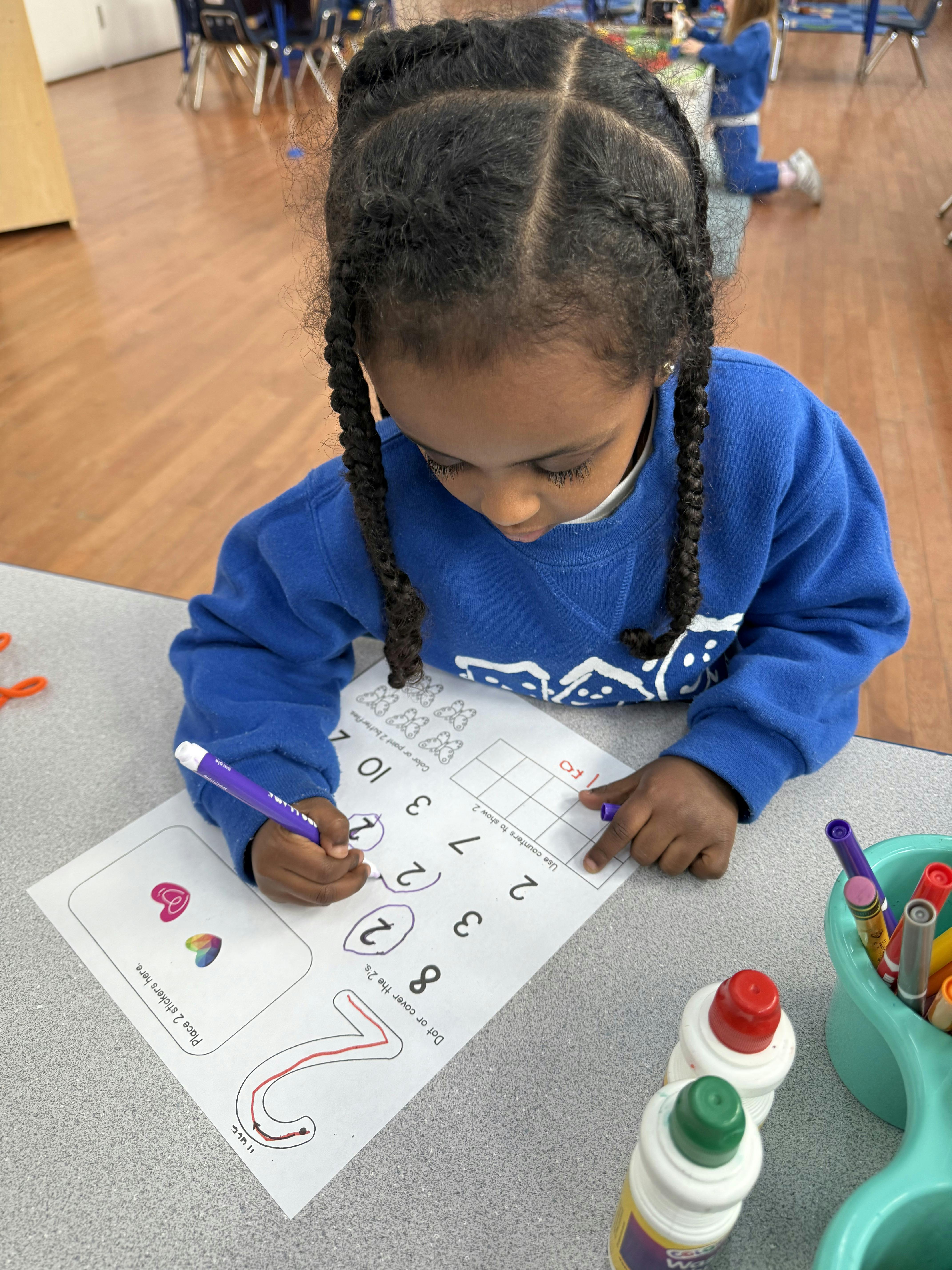 Child writing numbers on a worksheet in a classroom