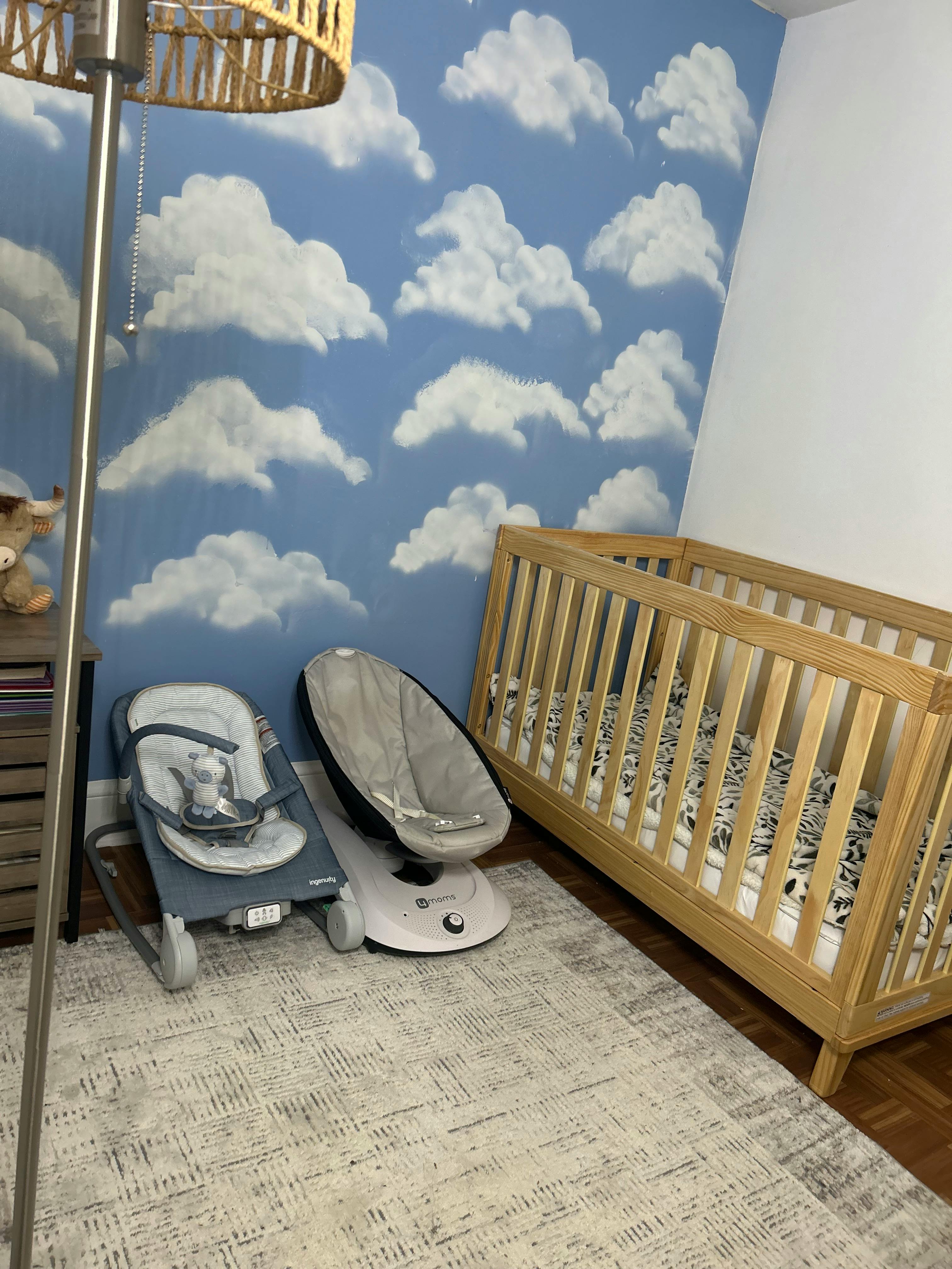 Baby nursery with cloud wallpaper, crib, and two baby bouncers