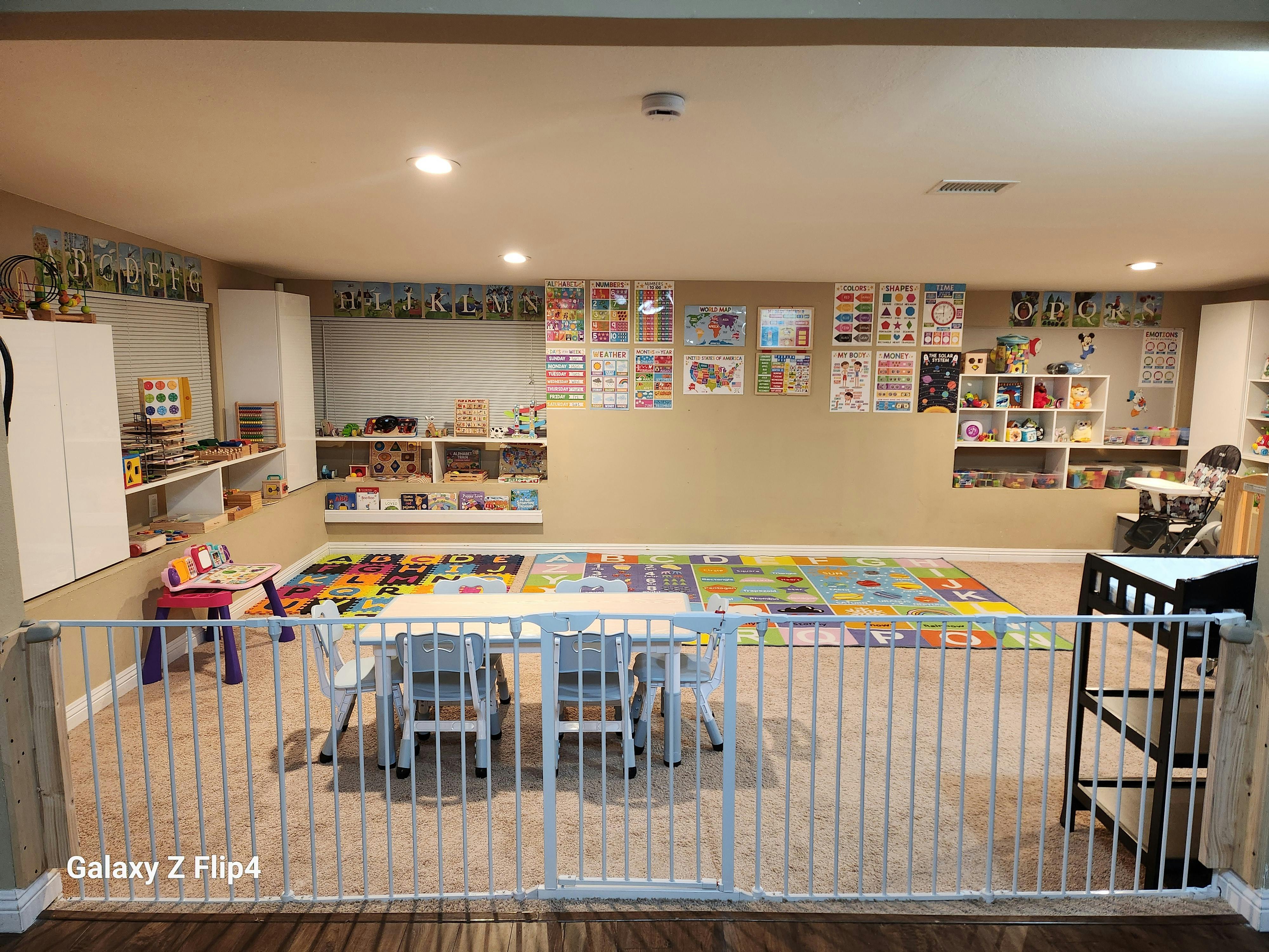 A child playroom with educational posters and activity tables behind a baby gate