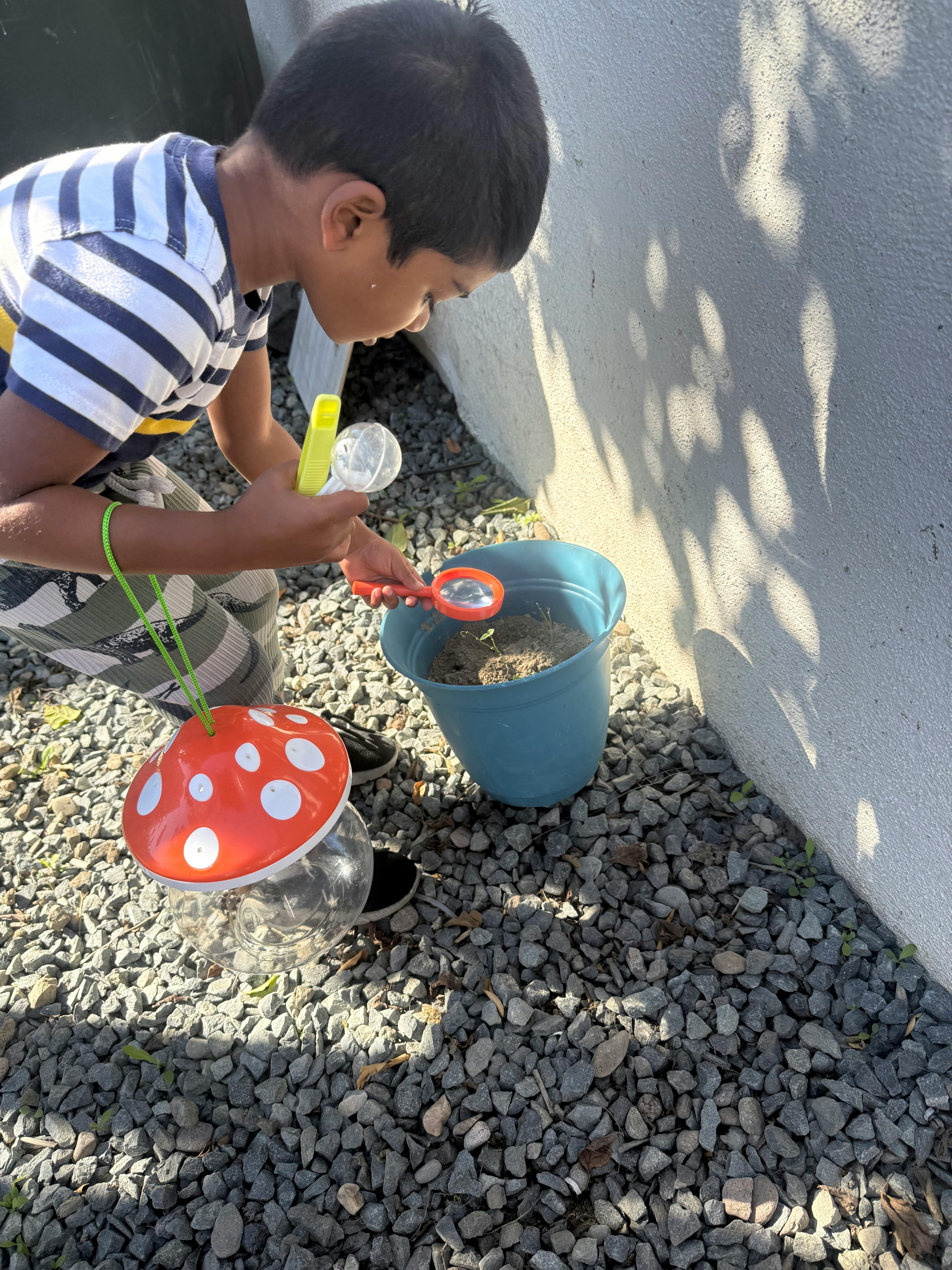 Child holding a magnifying glass and bug catcher, looking into a bucket