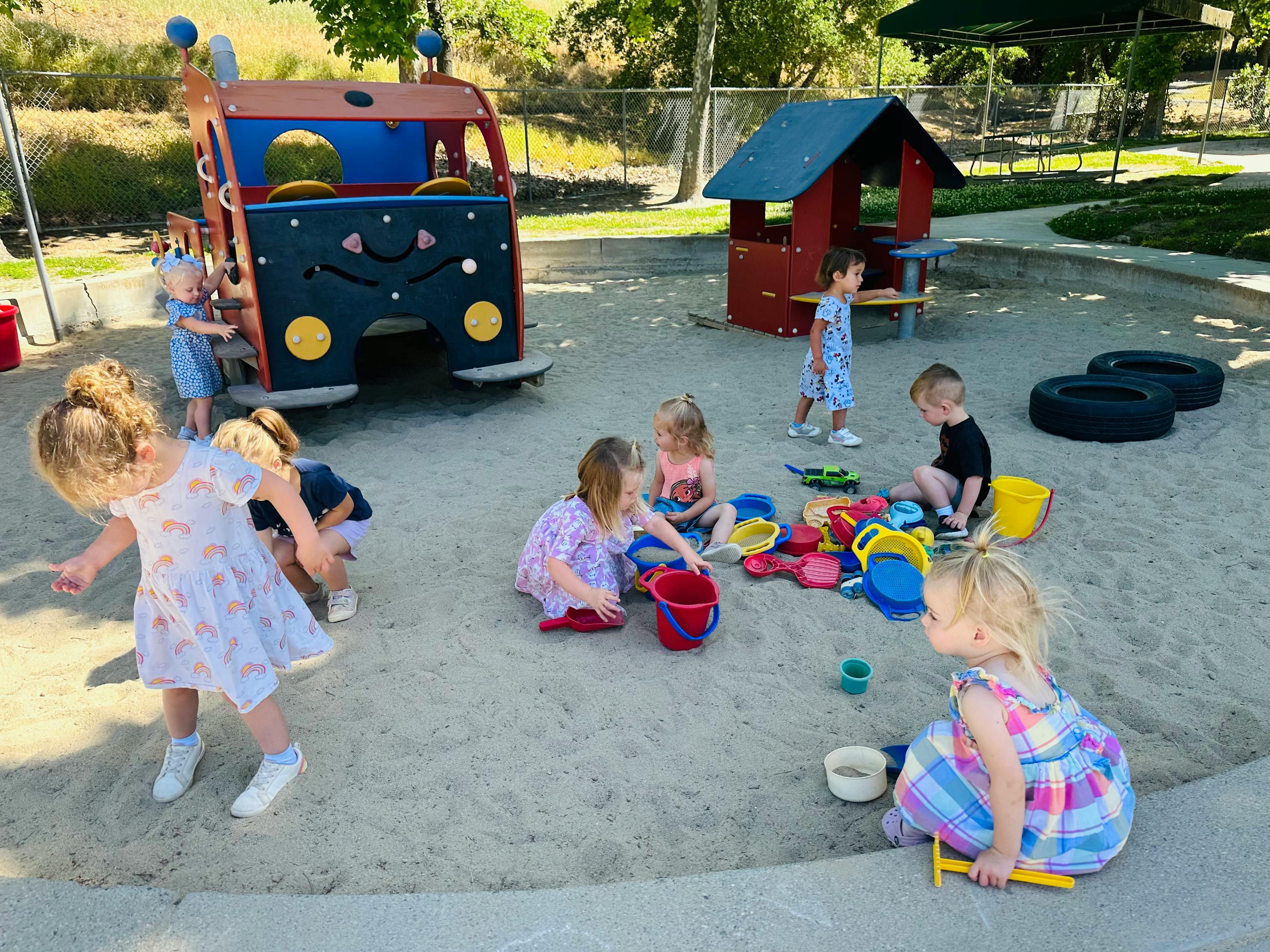 Children playing in a sandbox with toys and playground equipment