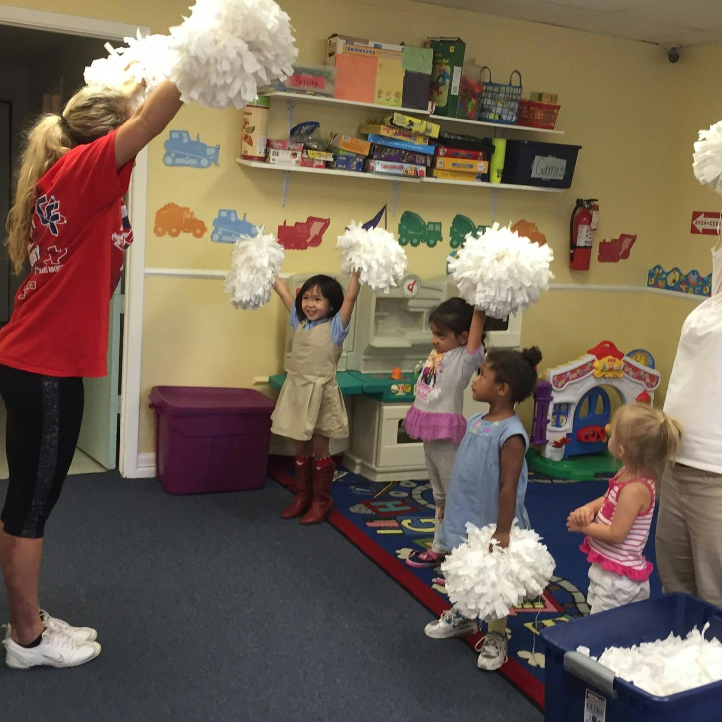 Person and children holding white pom-poms in a classroom