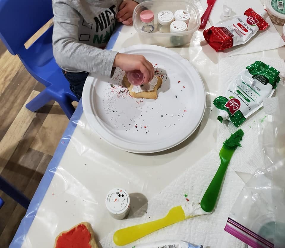 Child decorating a cookie with sprinkles on a white plate