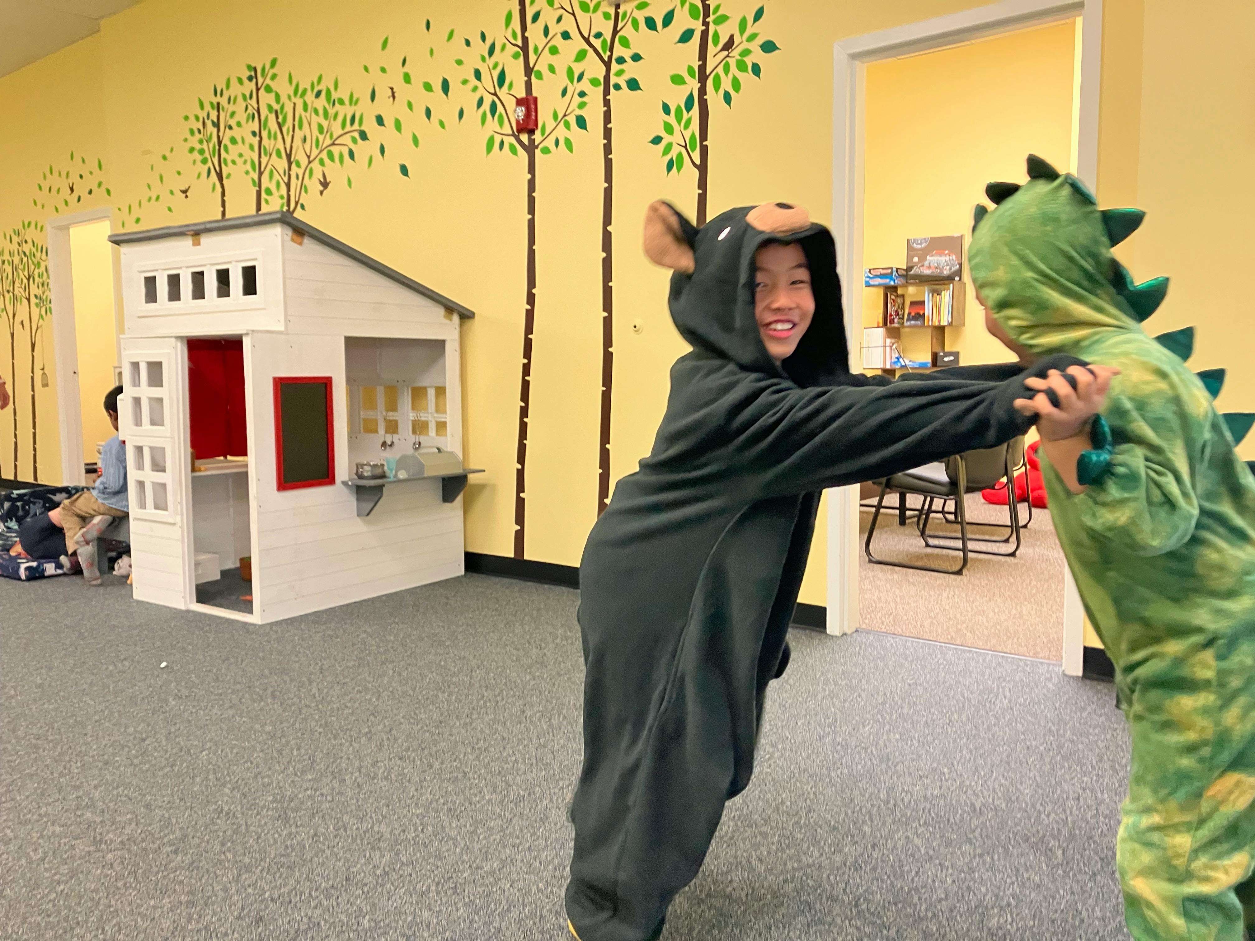 Child in bear costume playing with child in dinosaur costume
