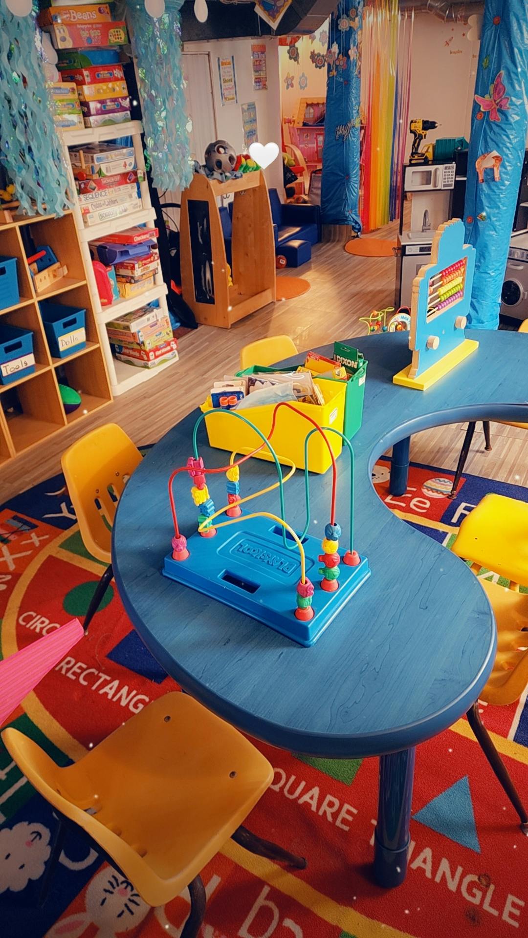 Classroom with a blue kidney-shaped table, chairs, and toys on a colorful rug