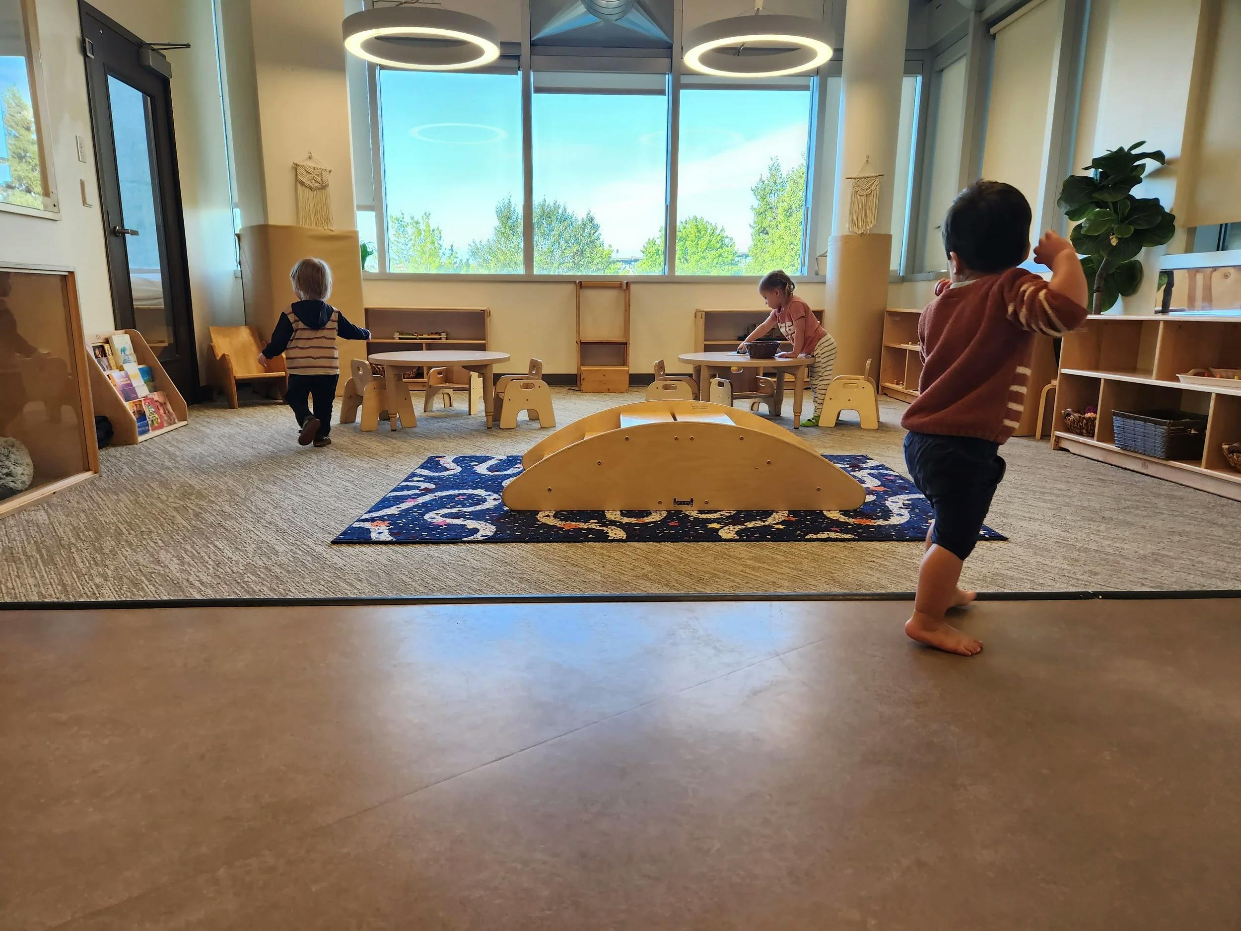 Three children in a classroom with large windows and play equipment