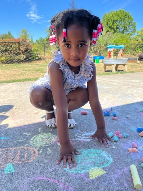Child crouching on pavement with chalk drawings