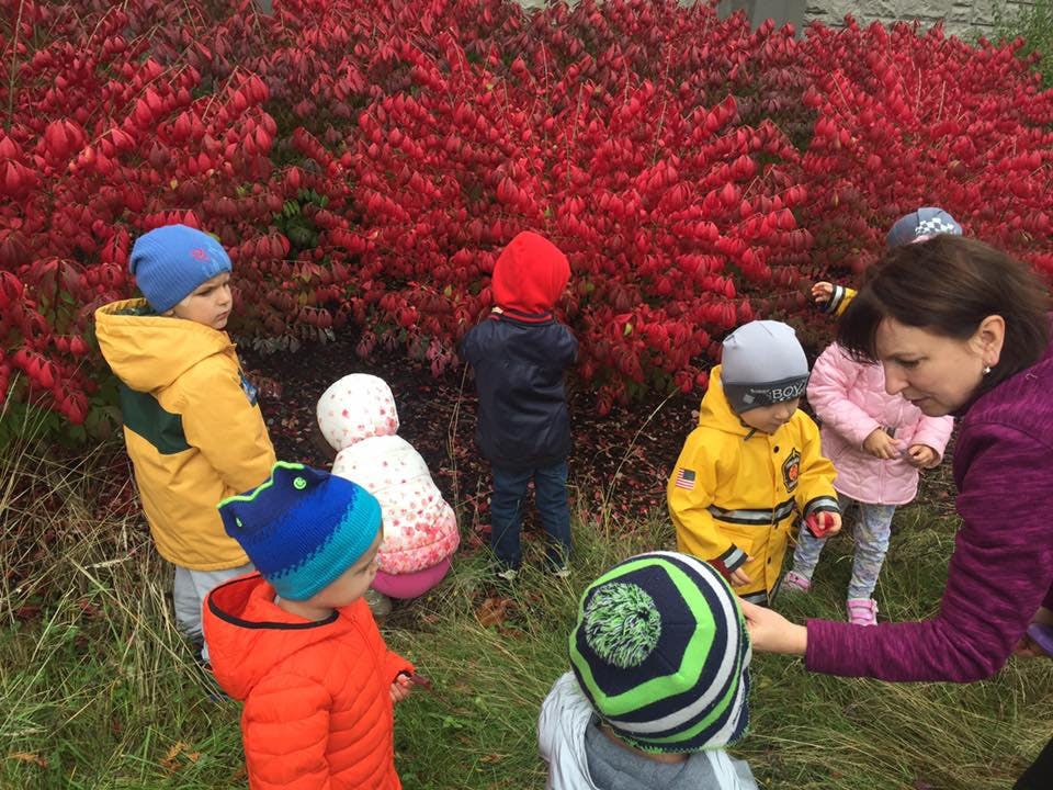 Adult and children outdoors near red bushes