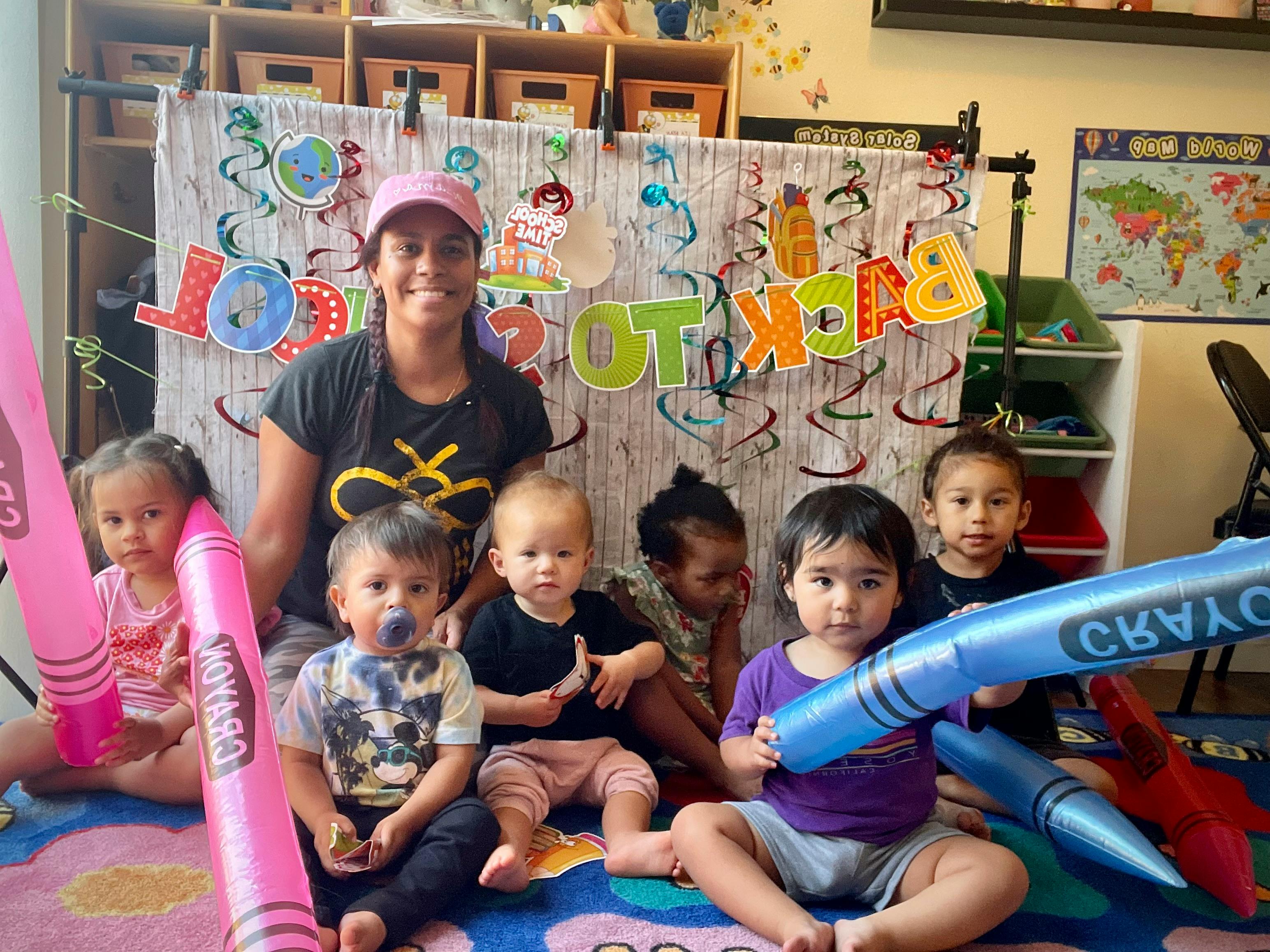 Person and multiple children sitting on a rug with inflatable crayons