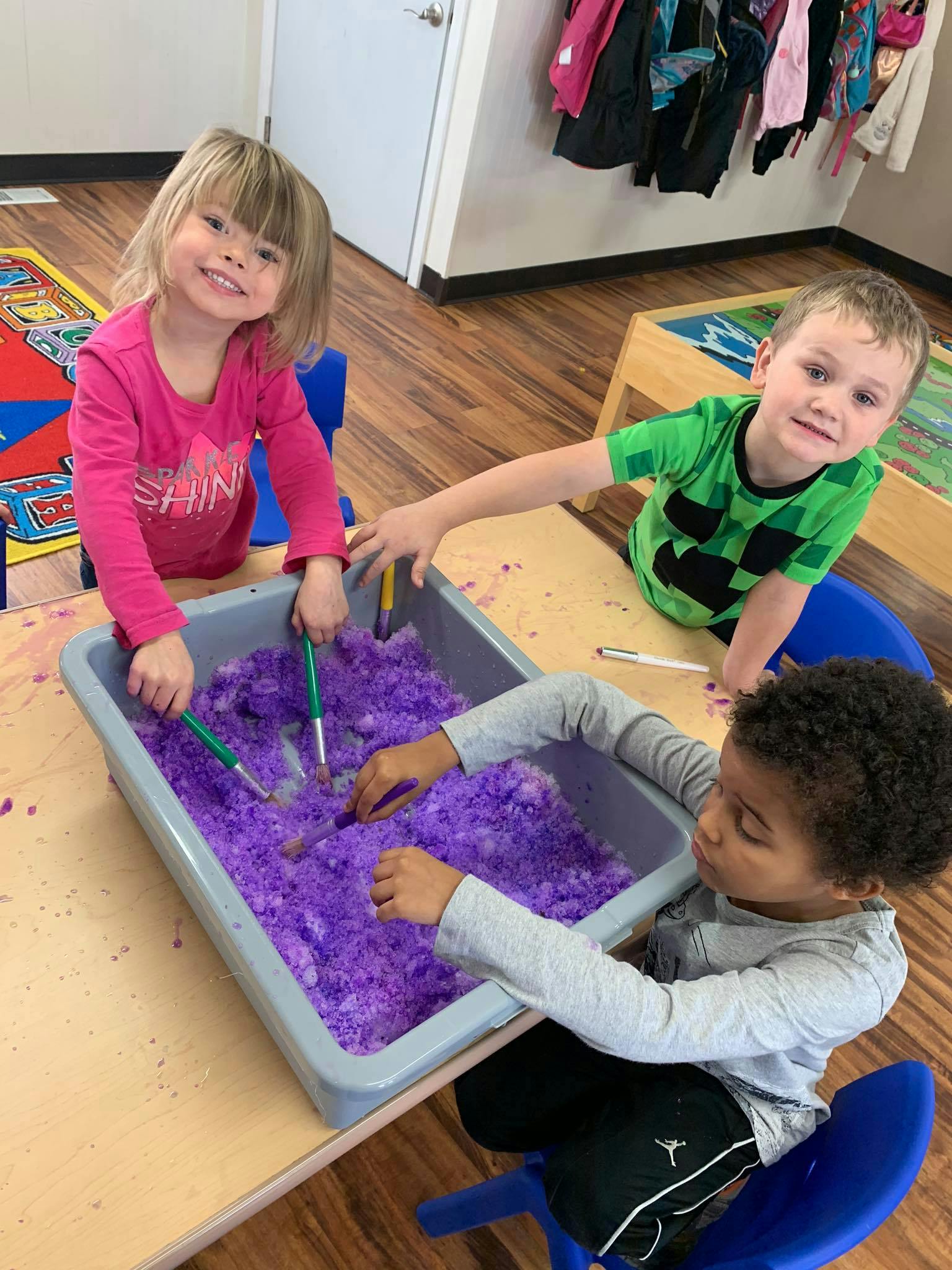 Three children playing with purple sensory bin filler in a bin