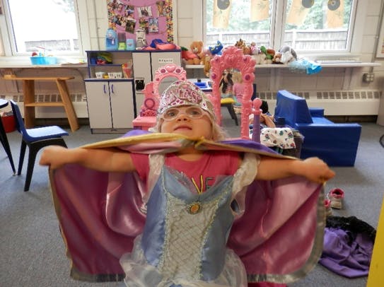 Child in a costume with a cape in a classroom