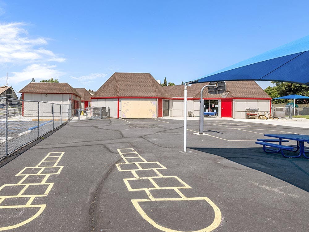 Playground with hopscotch, basketball hoop, picnic table, and school buildings