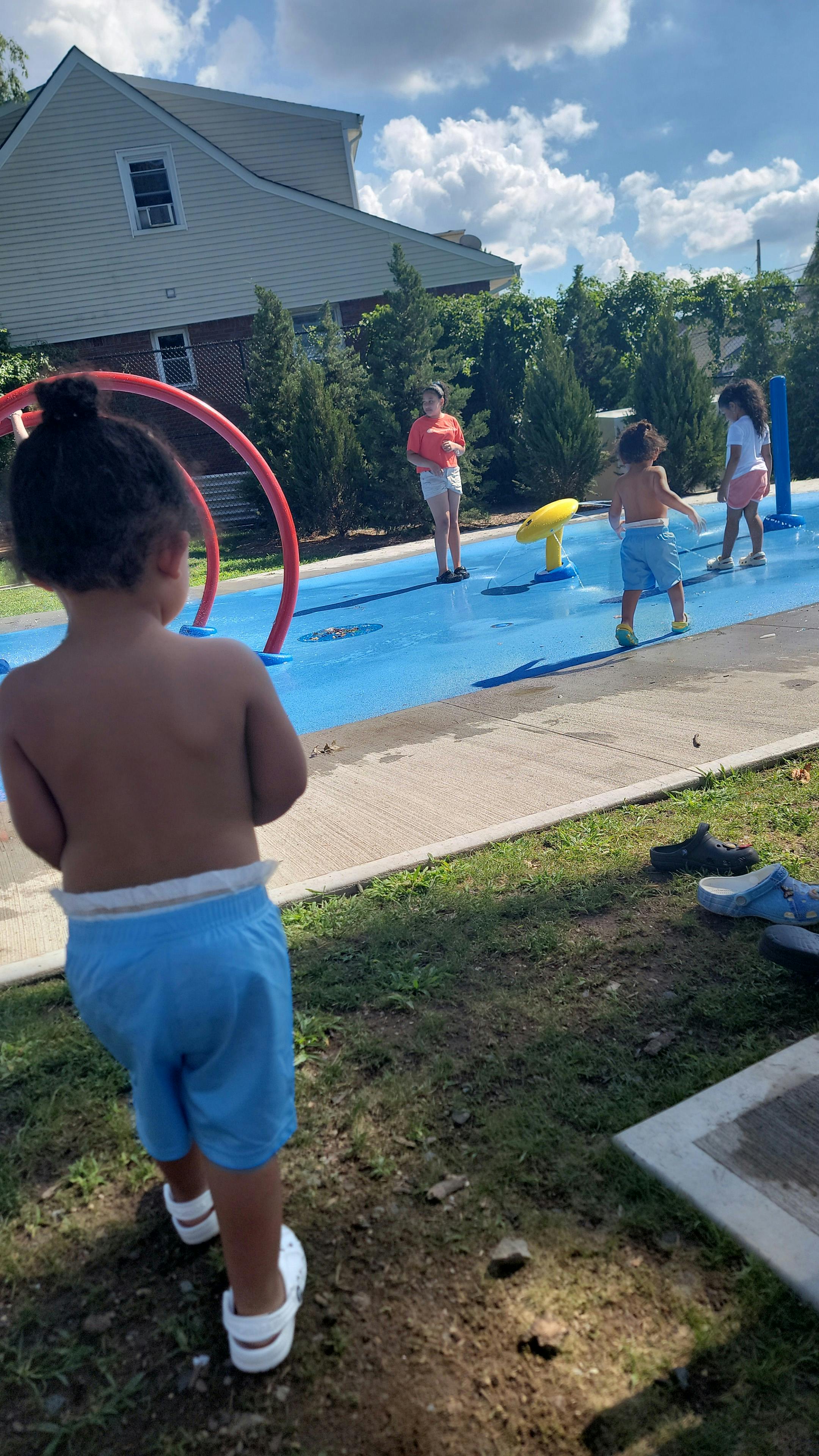 Child in blue shorts watching other children play in a splash pad