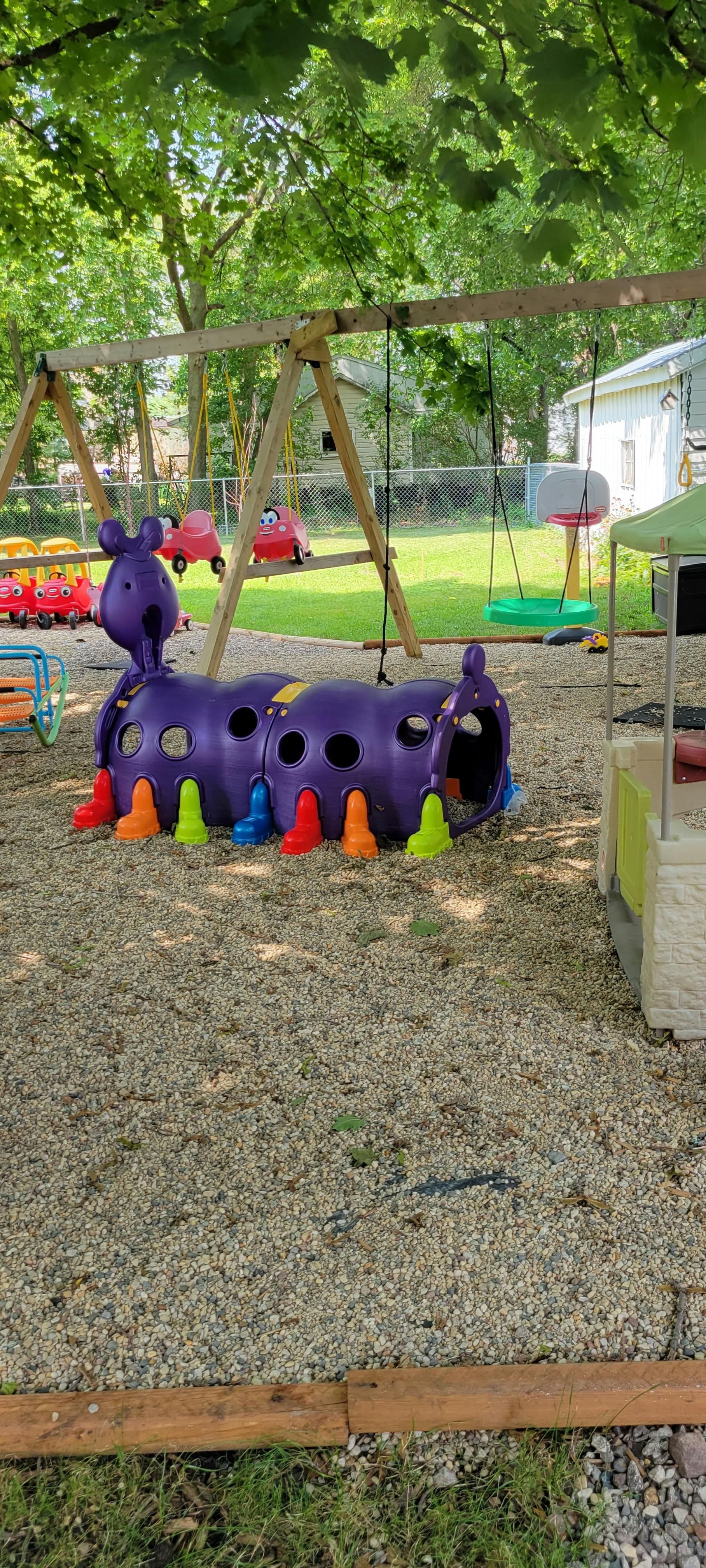 Purple caterpillar tunnel on a playground with swings and ride-on toys