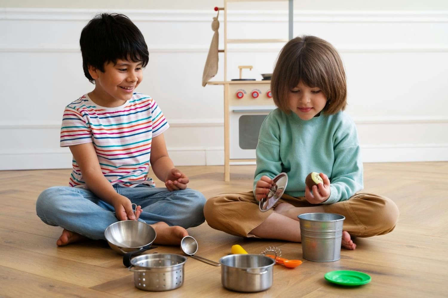 Two children sitting on the floor playing with toy kitchenware