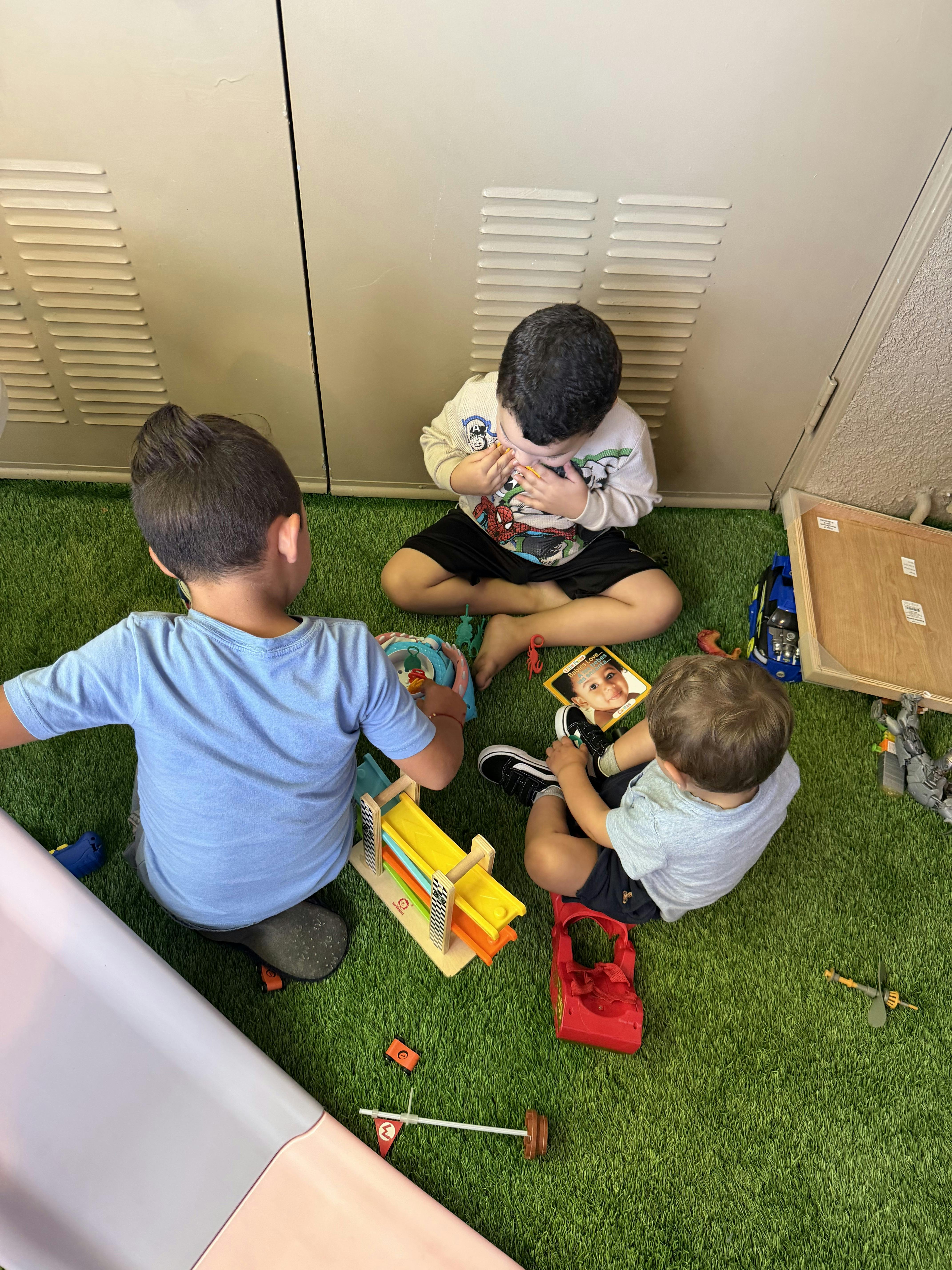 Three children playing with toys on green artificial grass