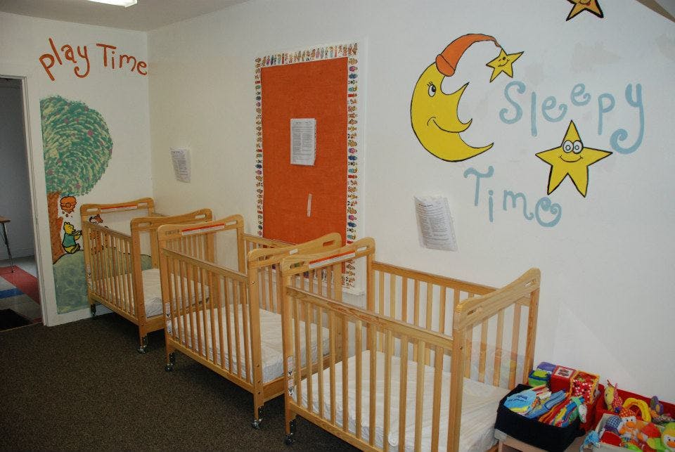Row of wooden cribs in a room with "Sleepy Time" painted on the wall