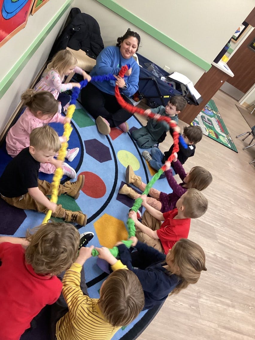 A person and several children sitting on a rug, holding and playing with colorful tubes