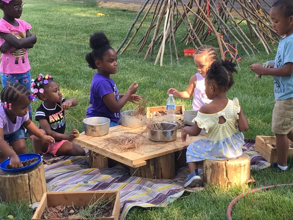 Children playing with natural materials at a low wooden table outdoors