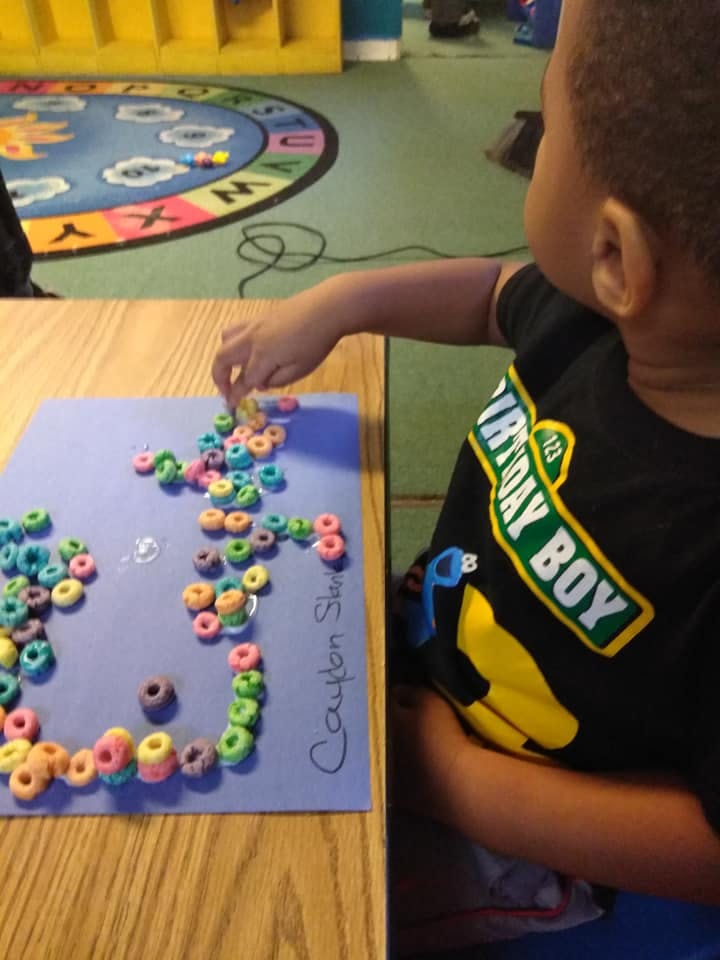 Child arranging colorful cereal pieces on a purple paper