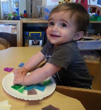Child playing with paper shapes on a plate at a table