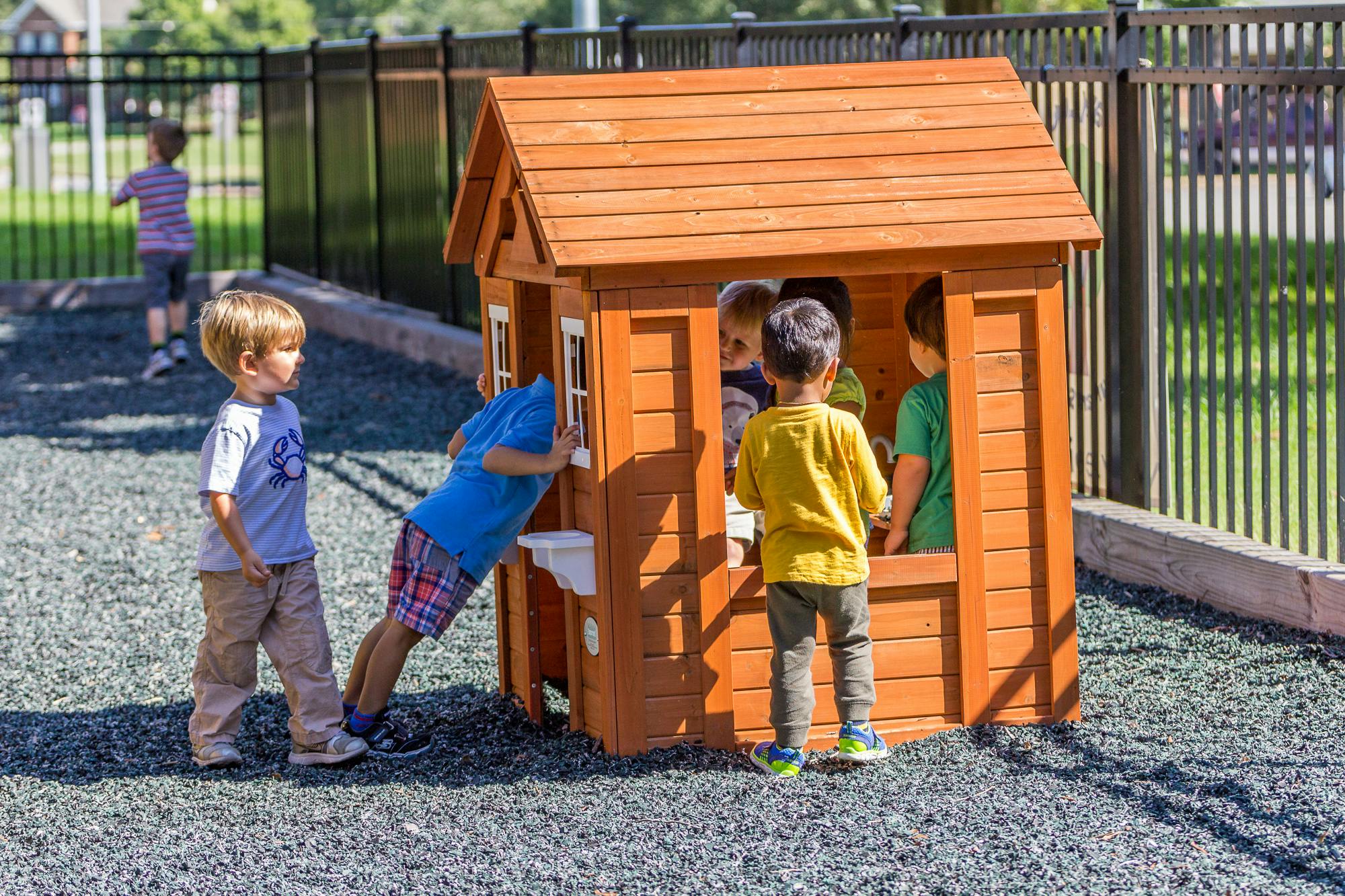 Children playing in and around a wooden playhouse on a playground