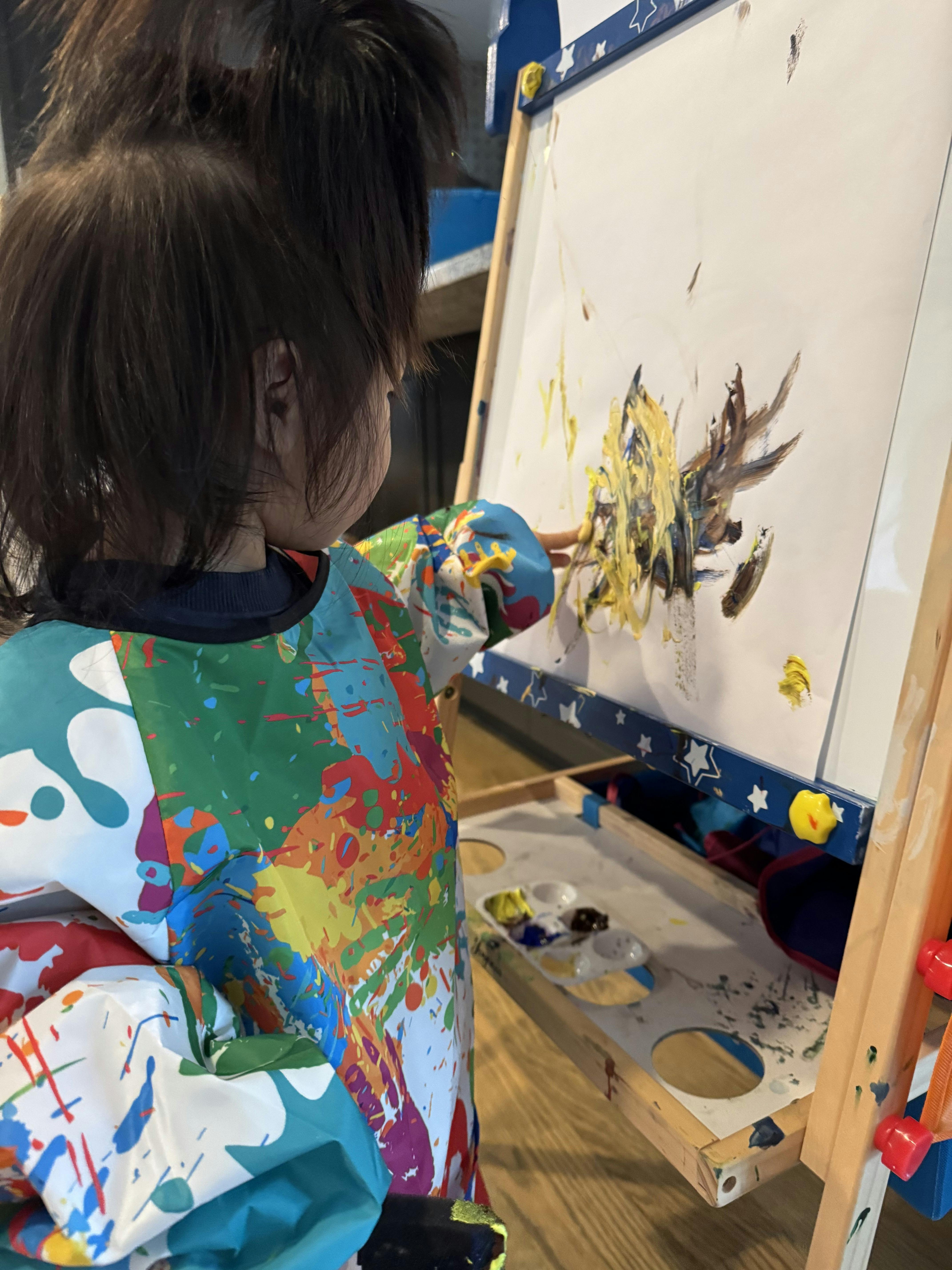 Child in a paint-splattered smock painting on an easel