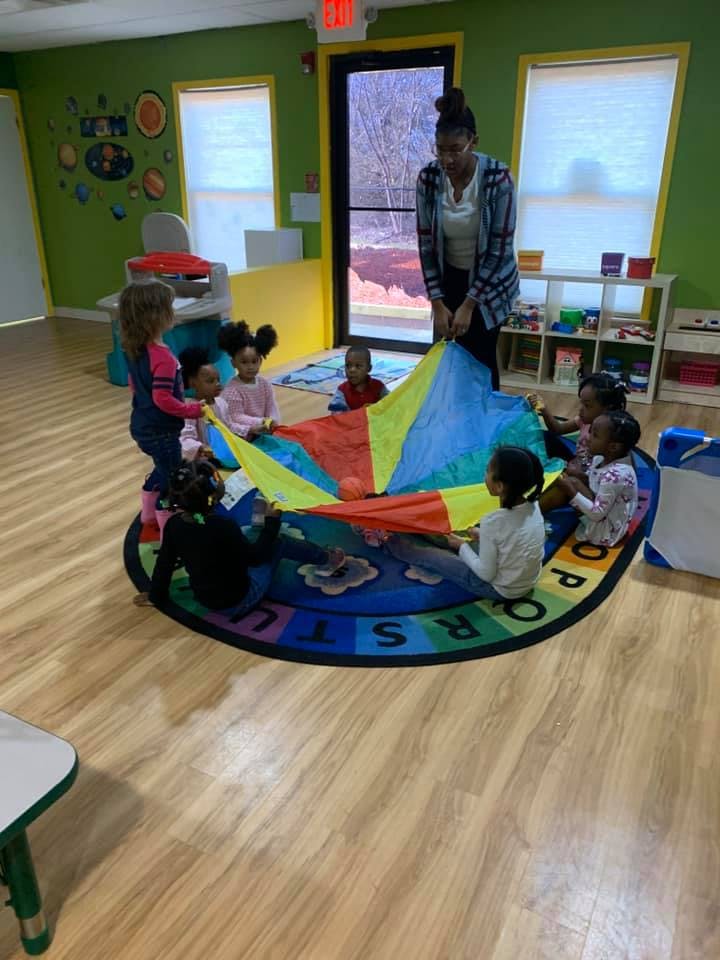 Adult and children playing with a colorful parachute in a classroom