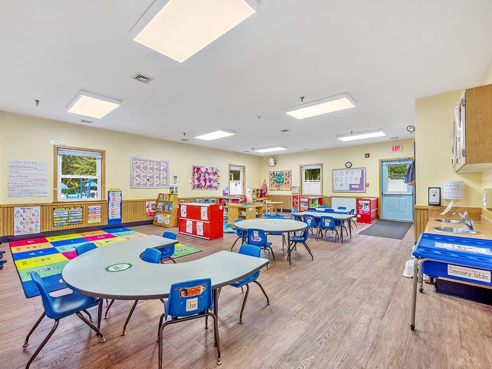 Empty classroom with tables, chairs, and colorful rug