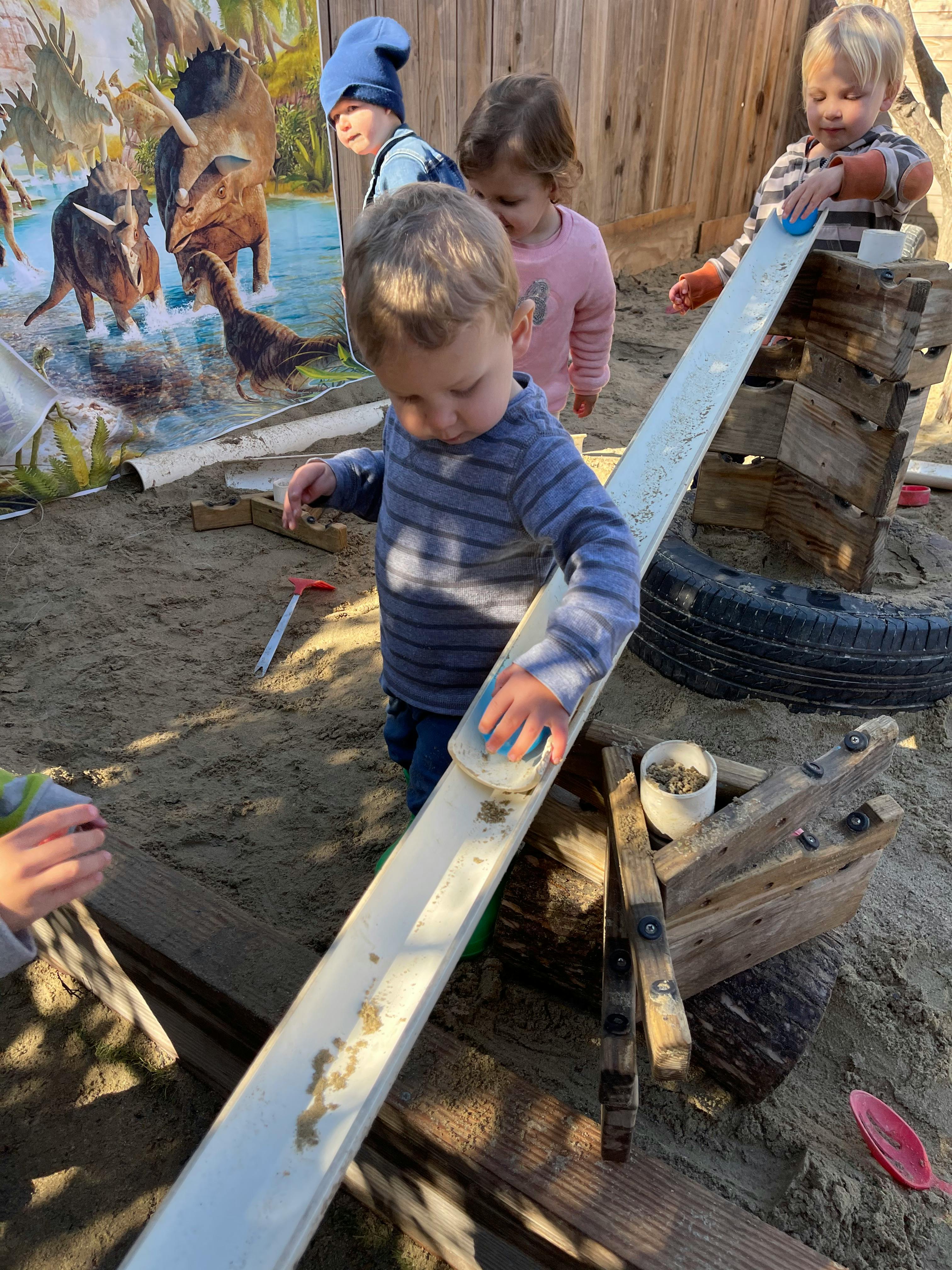 Children playing with a long white ramp in a sandy area