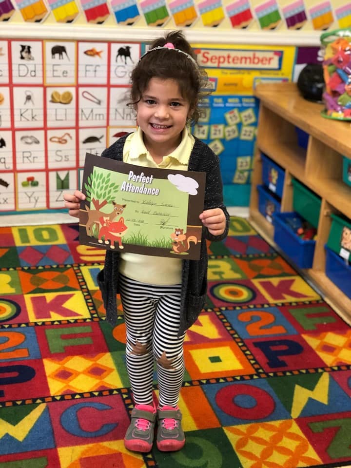 Child holding a Perfect Attendance certificate in a classroom