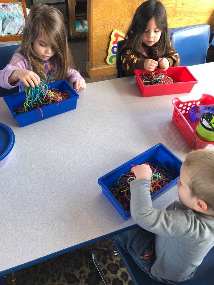 Three children playing with colorful rubber bands in containers