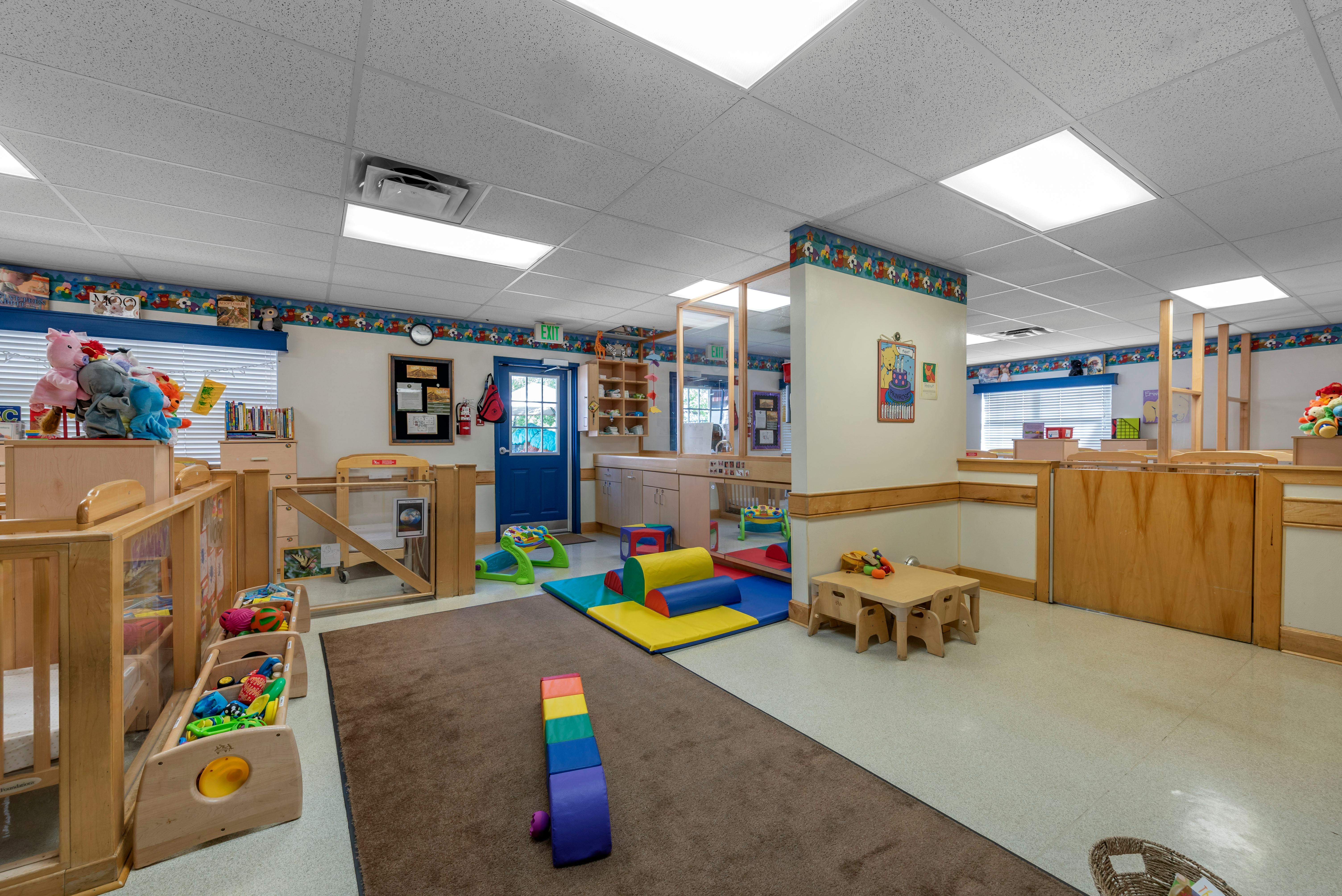 A childcare center classroom with play mats, low tables, and cribs