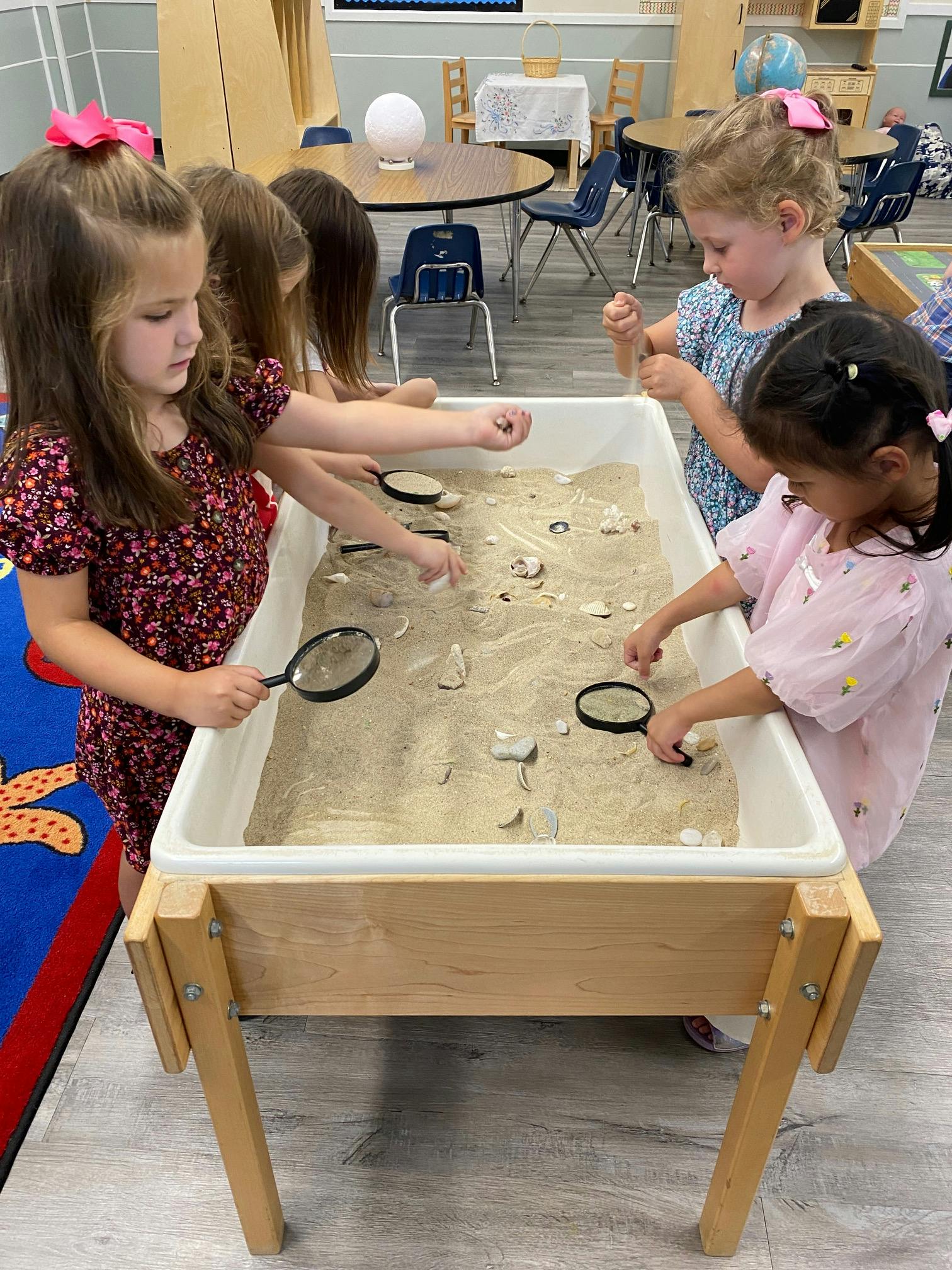 Children playing with sand and magnifying glasses in a classroom