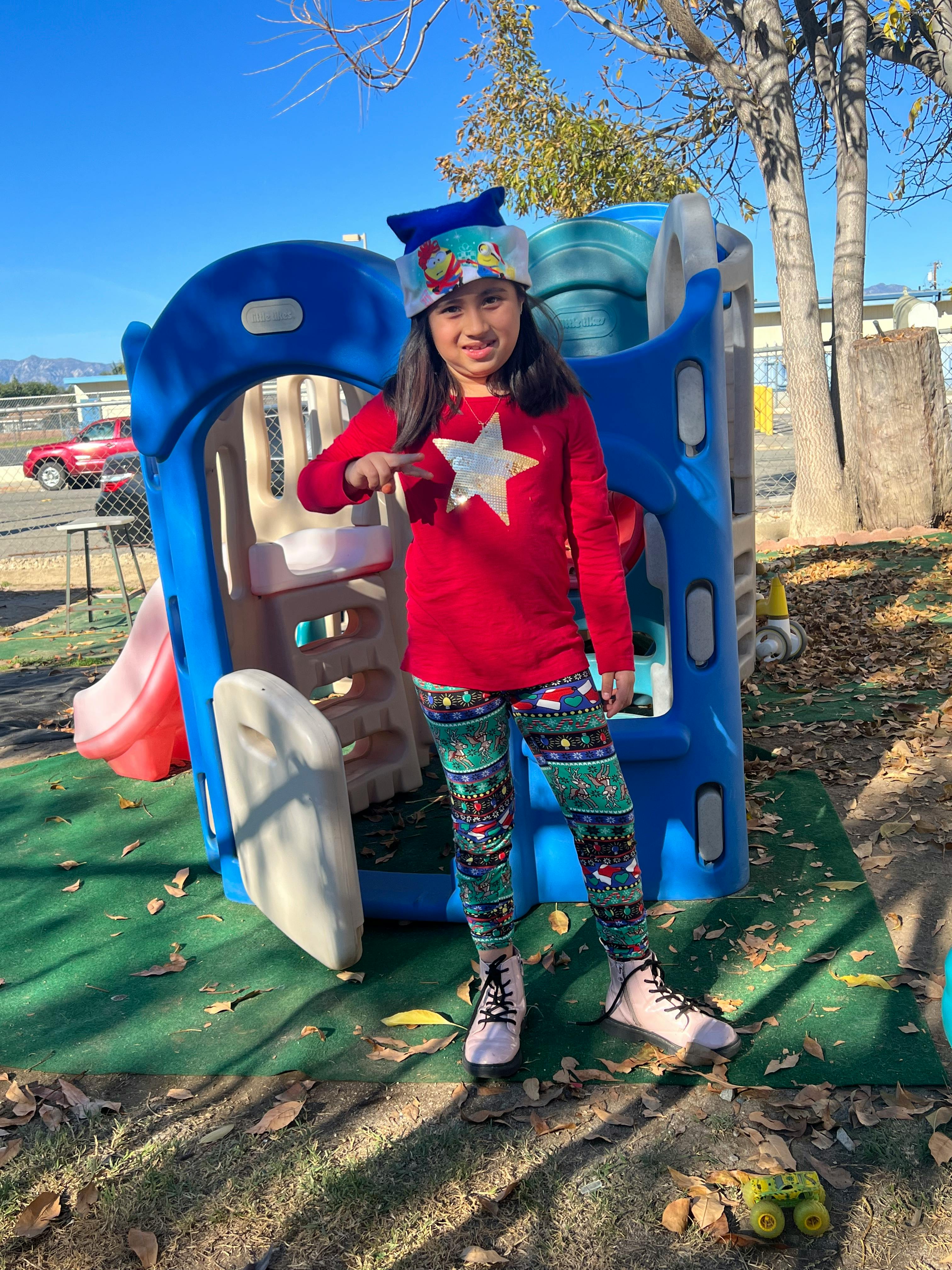 Child in a red shirt and patterned pants standing in front of a blue play structure