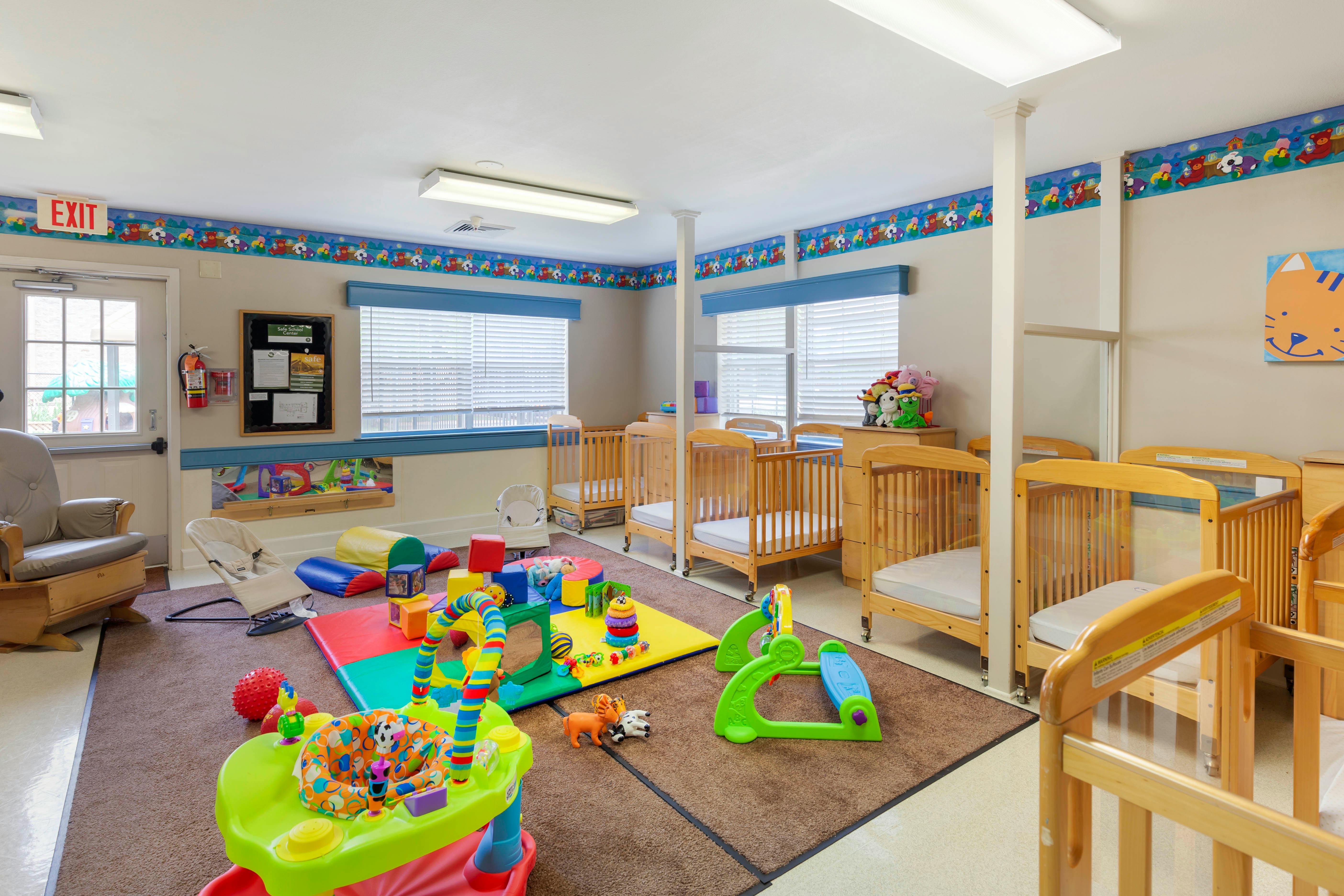 A colorful childcare room with cribs, play mats, and toys
