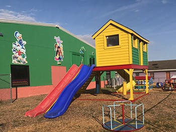 Playground with a yellow playhouse, red slide, blue slide, and merry-go-round