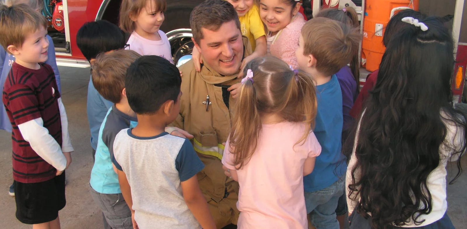 Firefighter kneeling with children gathered around