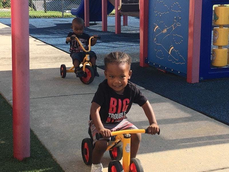 Two children riding tricycles on a paved surface