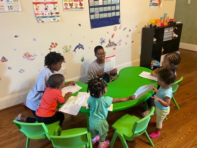 Adult and multiple children sitting around a green table with papers