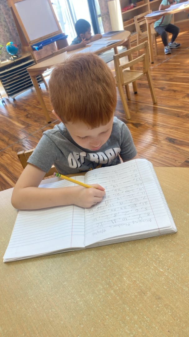 Child writing in a notebook with a pencil in a classroom