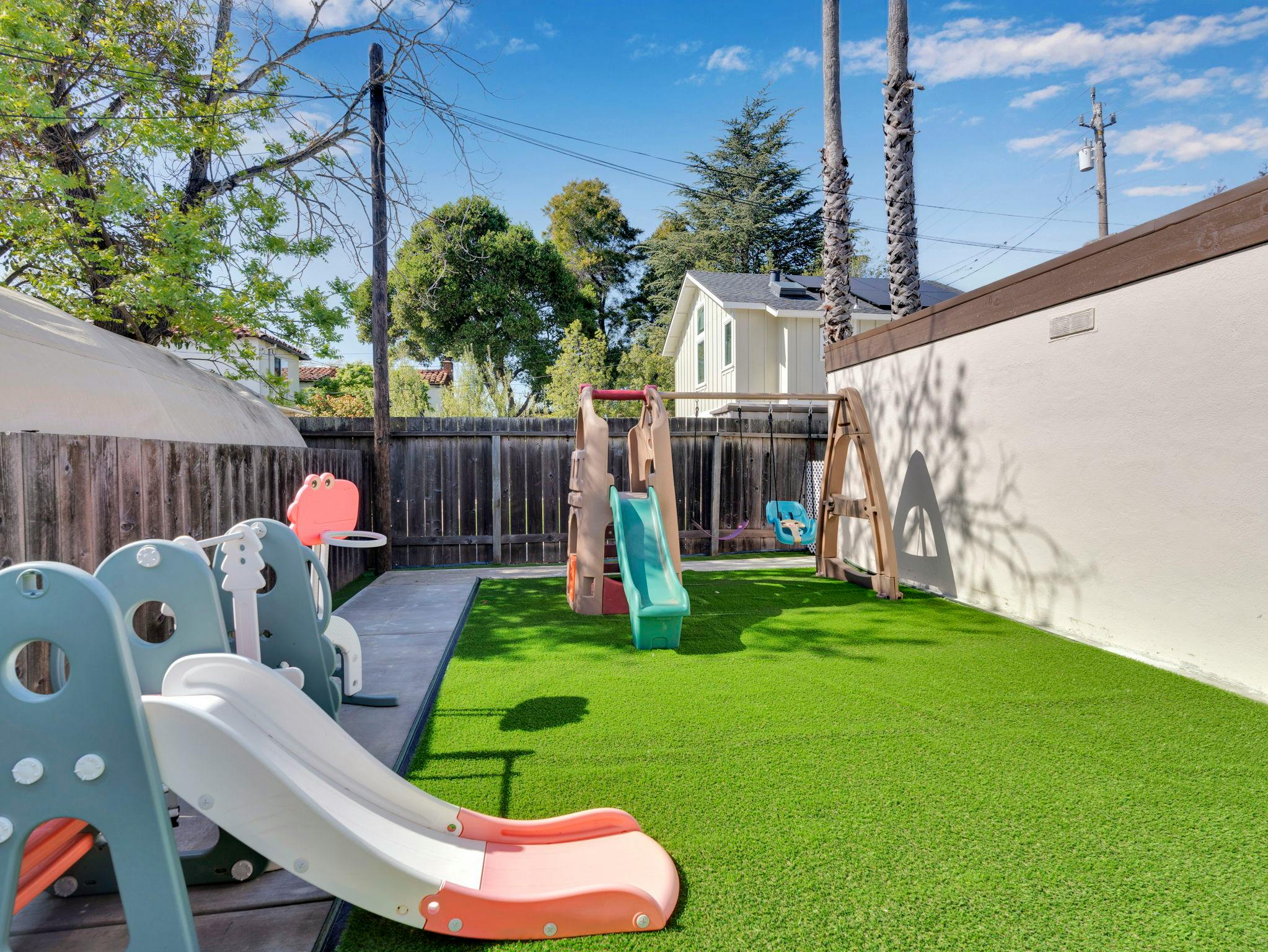 Backyard with artificial turf, two slides, and a swing set