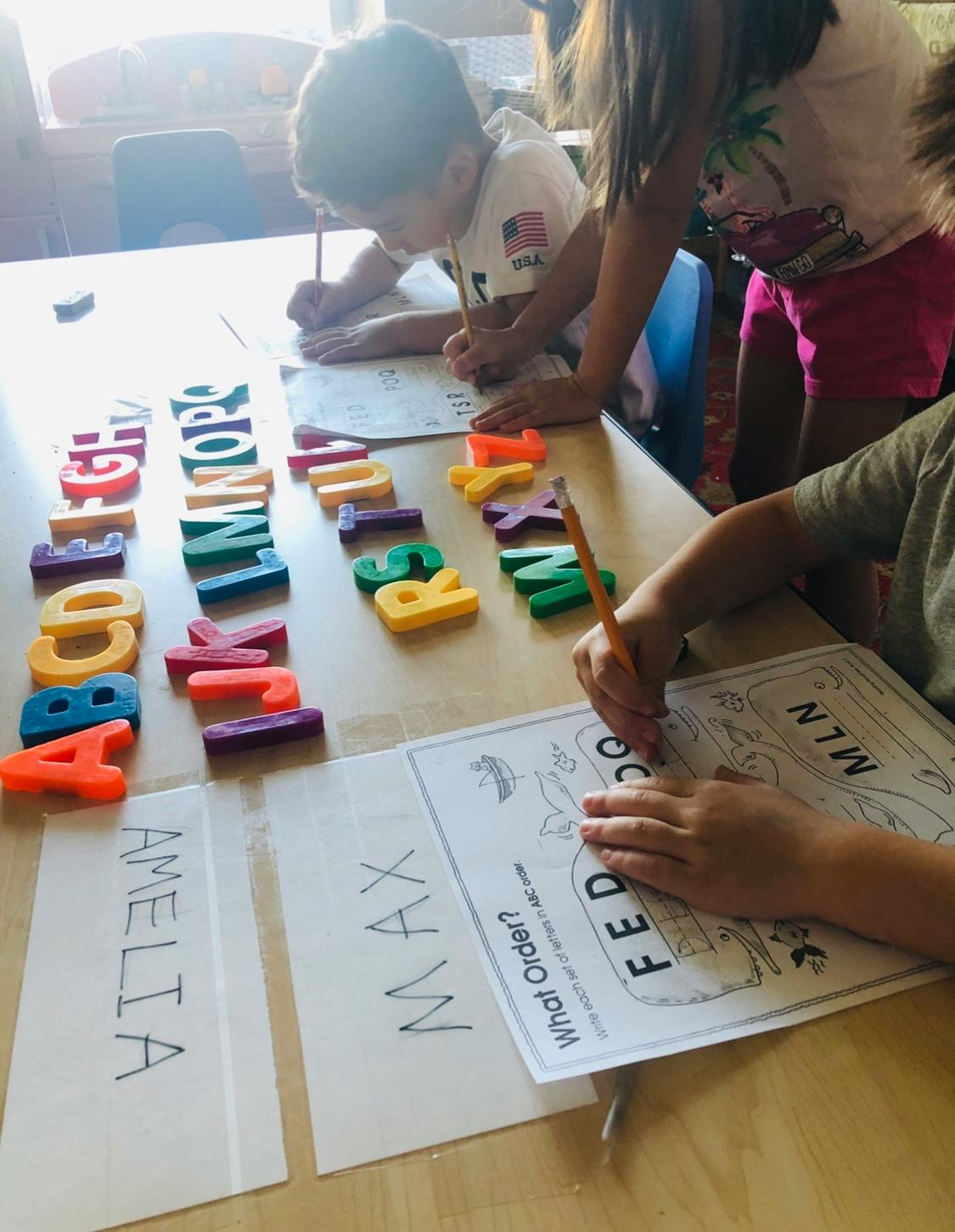 Children writing and arranging alphabet letters on a table